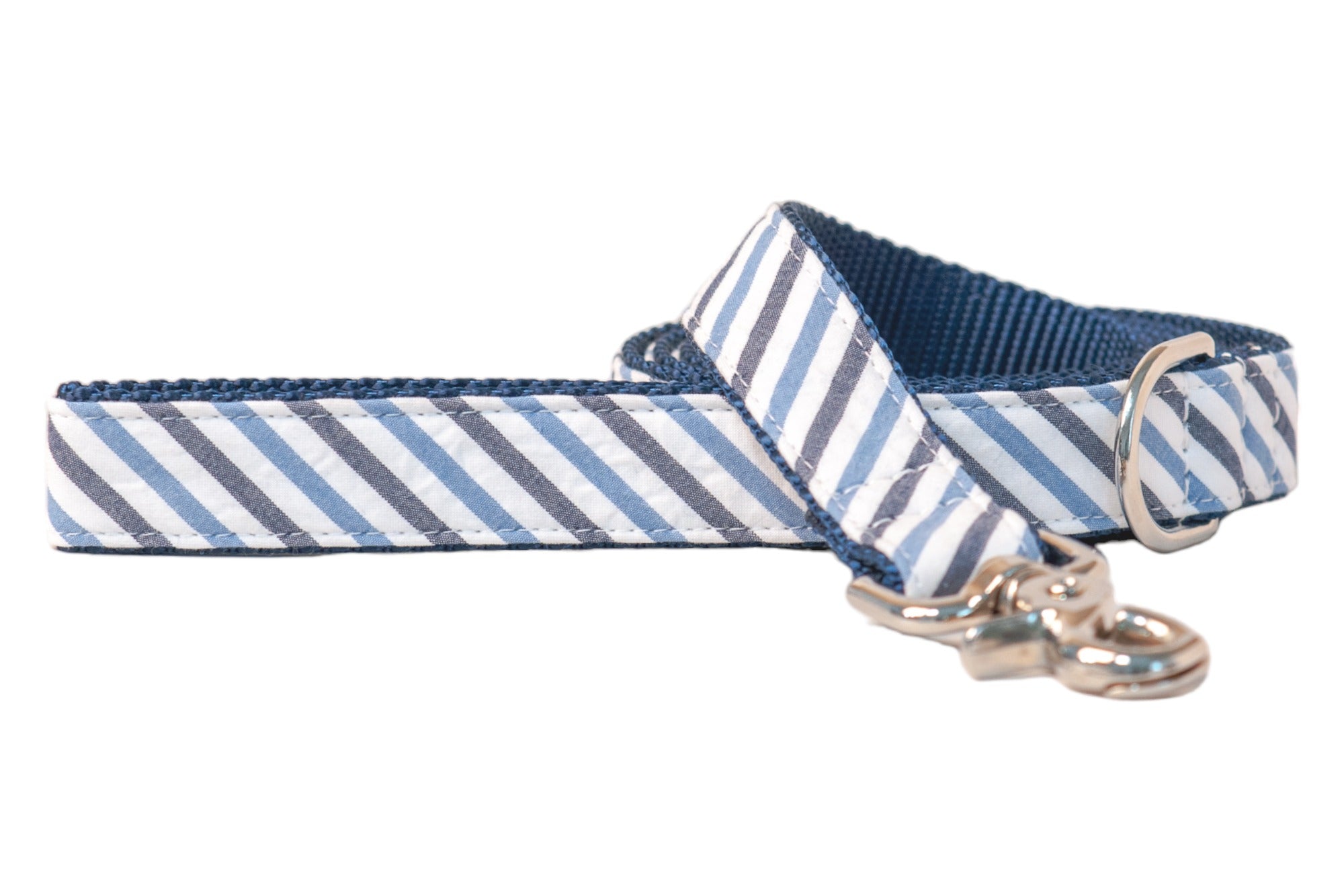 Stylish dog leash with navy, blue, and white striped seersucker on the outer side, backed with sturdy navy webbing. The leash is shown partially coiled and features sleek silver metal hardware, including a swivel hook clip and a D-ring for attachments. The design blends a nautical theme with functional pet gear.