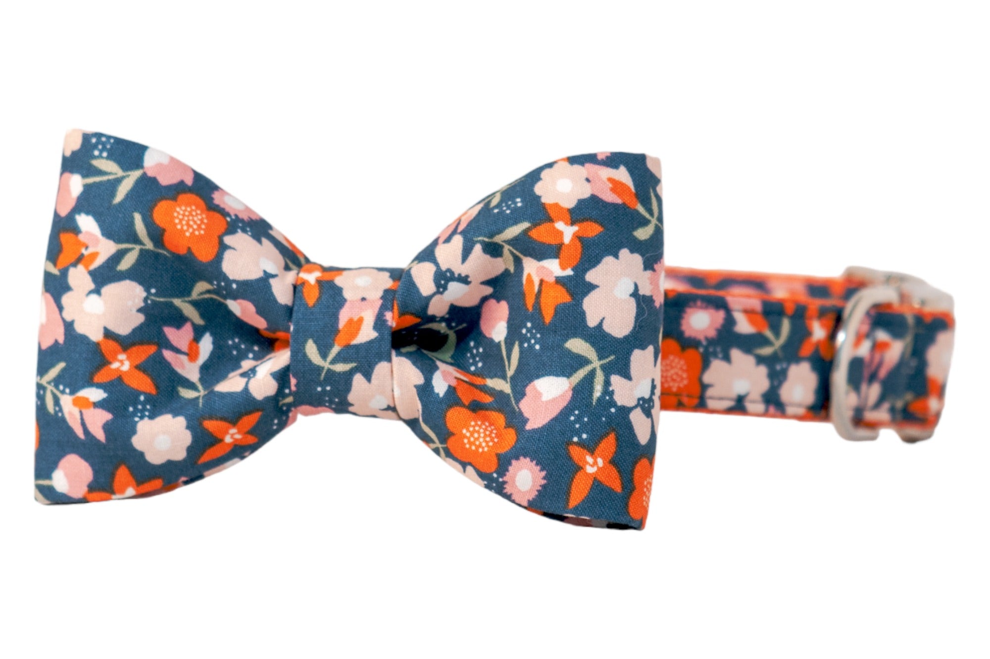 Close-up of a dog bow tie collar in a vibrant floral print on dark fabric, decorated with blossoms along with leafy stems. The structured bow tie is attached to the collar, and features polished hardware and neat topstitching along the edges, both in matching fabric.