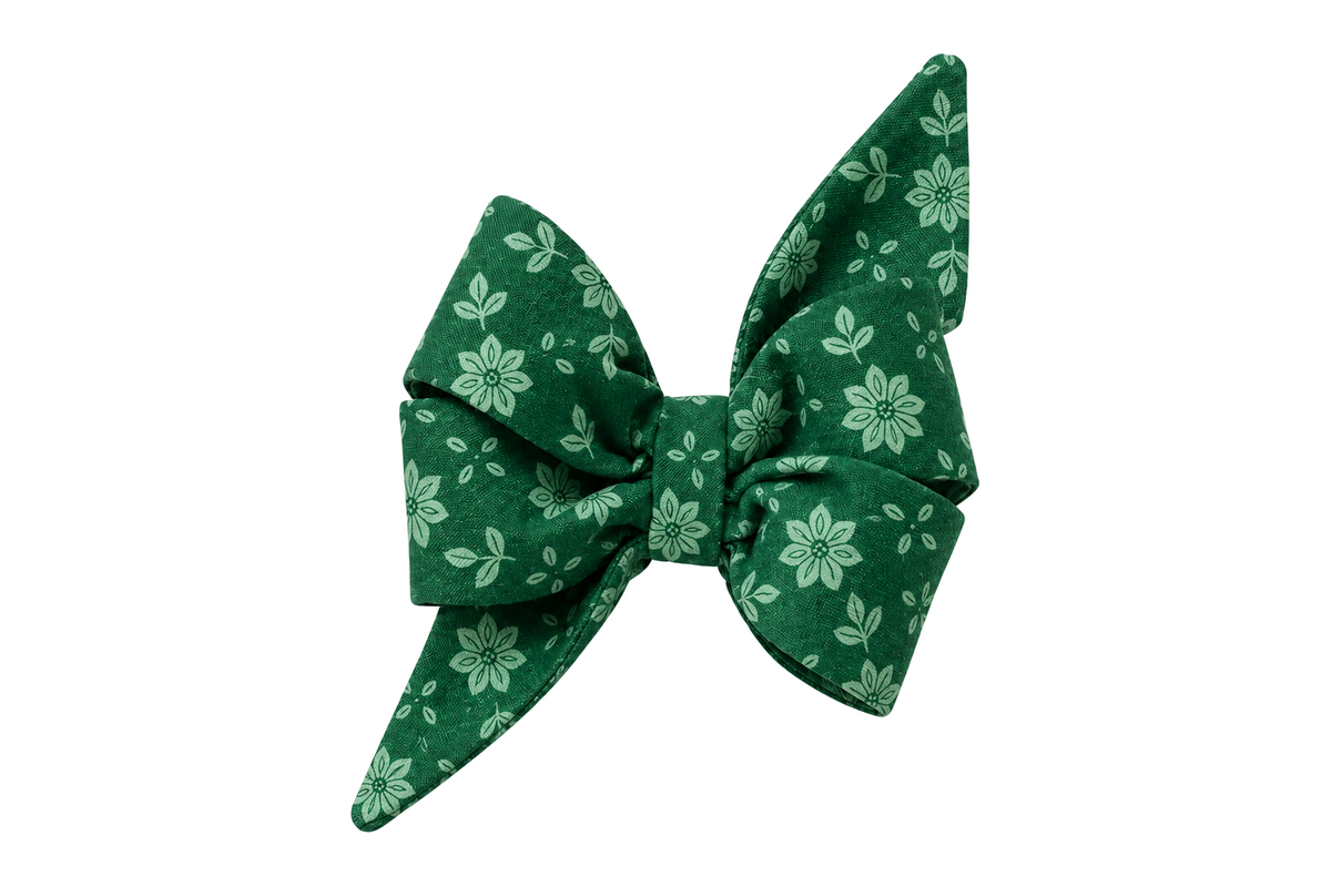 Standalone belle bow in Basil Blooms fabric, a deep forest green print with soft light green poinsettia flowers and leaves, with full upright loops and two pointed tails, photographed on a white studio background.