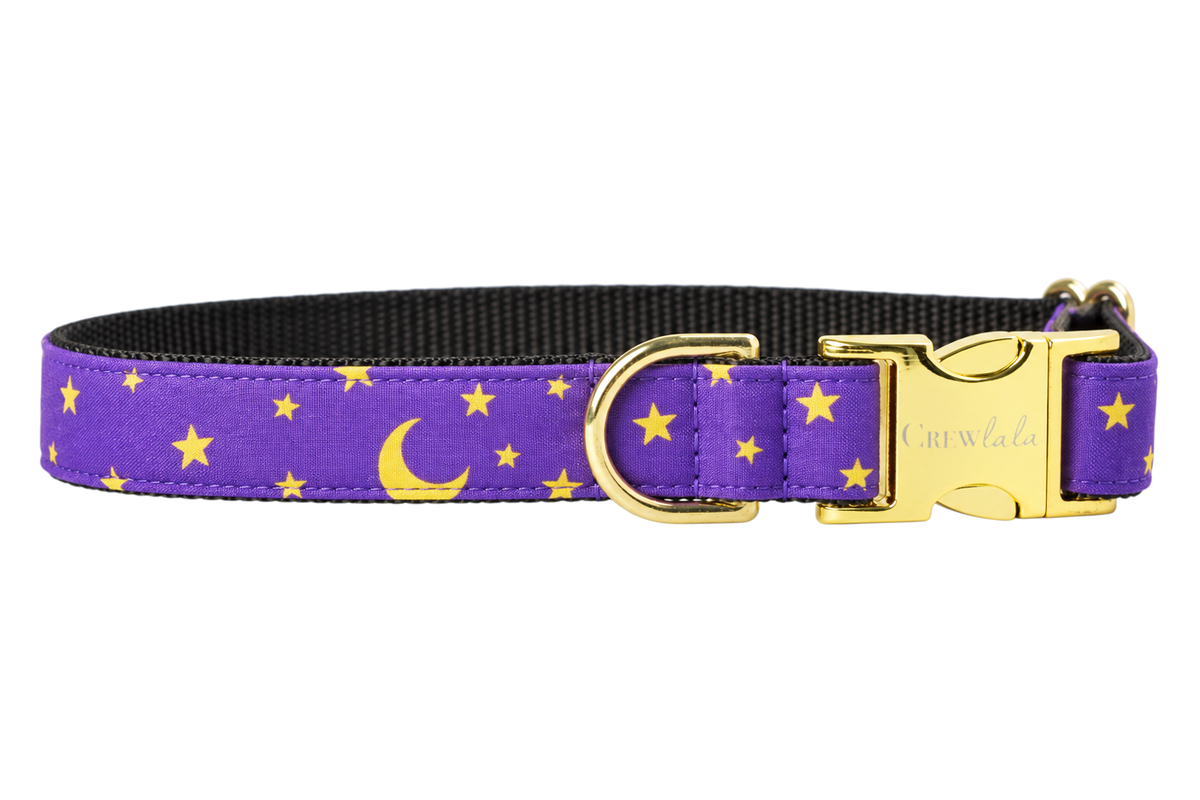Plain Bewitched dog collar without the bow, made with a purple fabric with golden yellow crescent moons and small stars, lined with black nylon webbing and gold hardware with a Crewlala logo buckle.