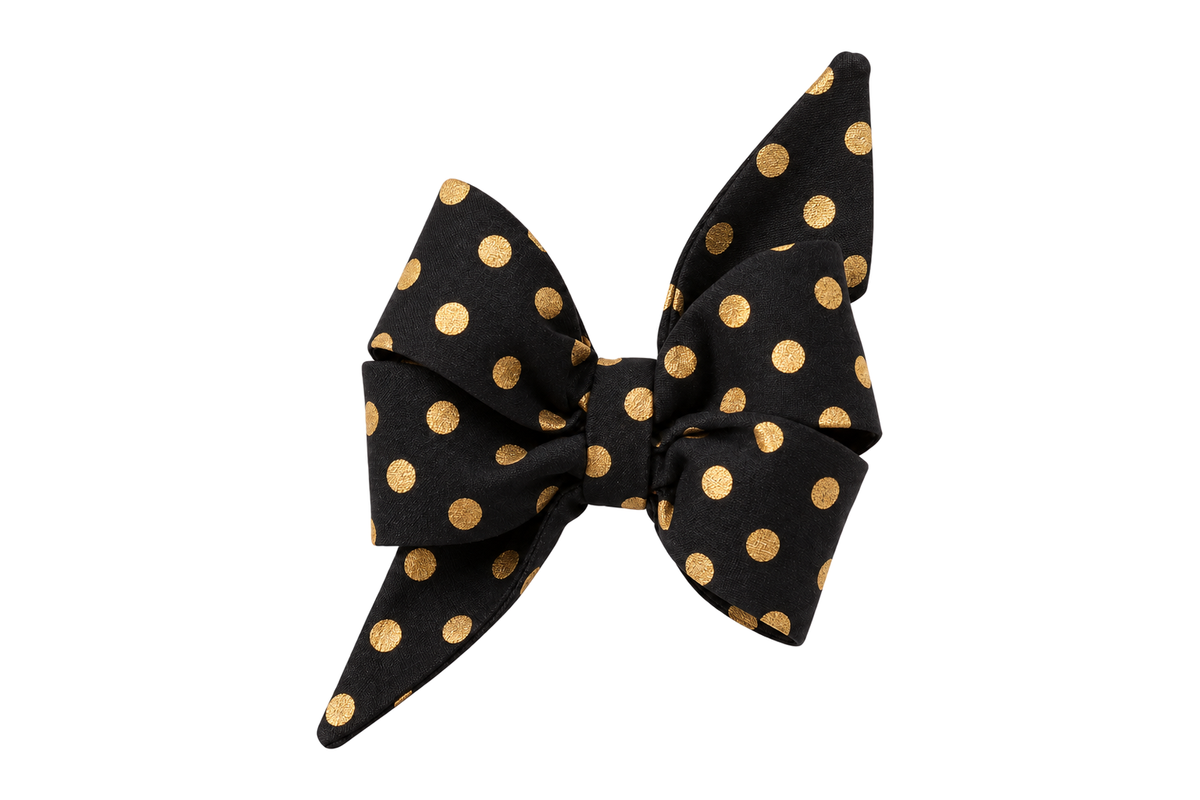 Standalone belle bow in Black Party Dot fabric, a black fabric with metallic gold polka dots, with full upright loops and two pointed tails, photographed on a white studio background.