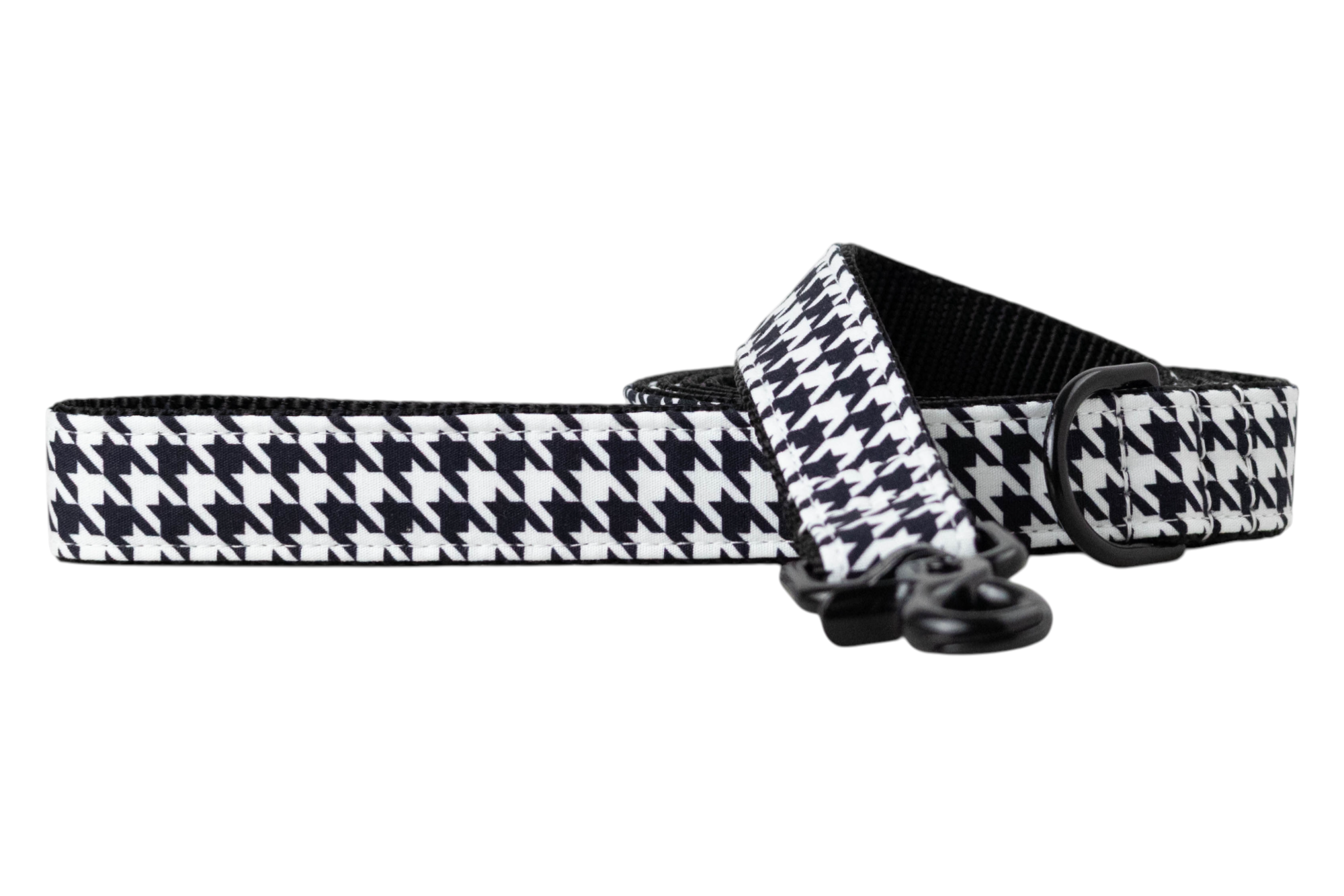 A dog leash with a black and white houndstooth fabric overlay, backed with sturdy black nylon webbing for durability. The leash is shown partially coiled and includes matte black hardware, including a swivel clasp and D-ring for secure attachment and accessory clips. A modern, stylish accessory for fashionable pets.
