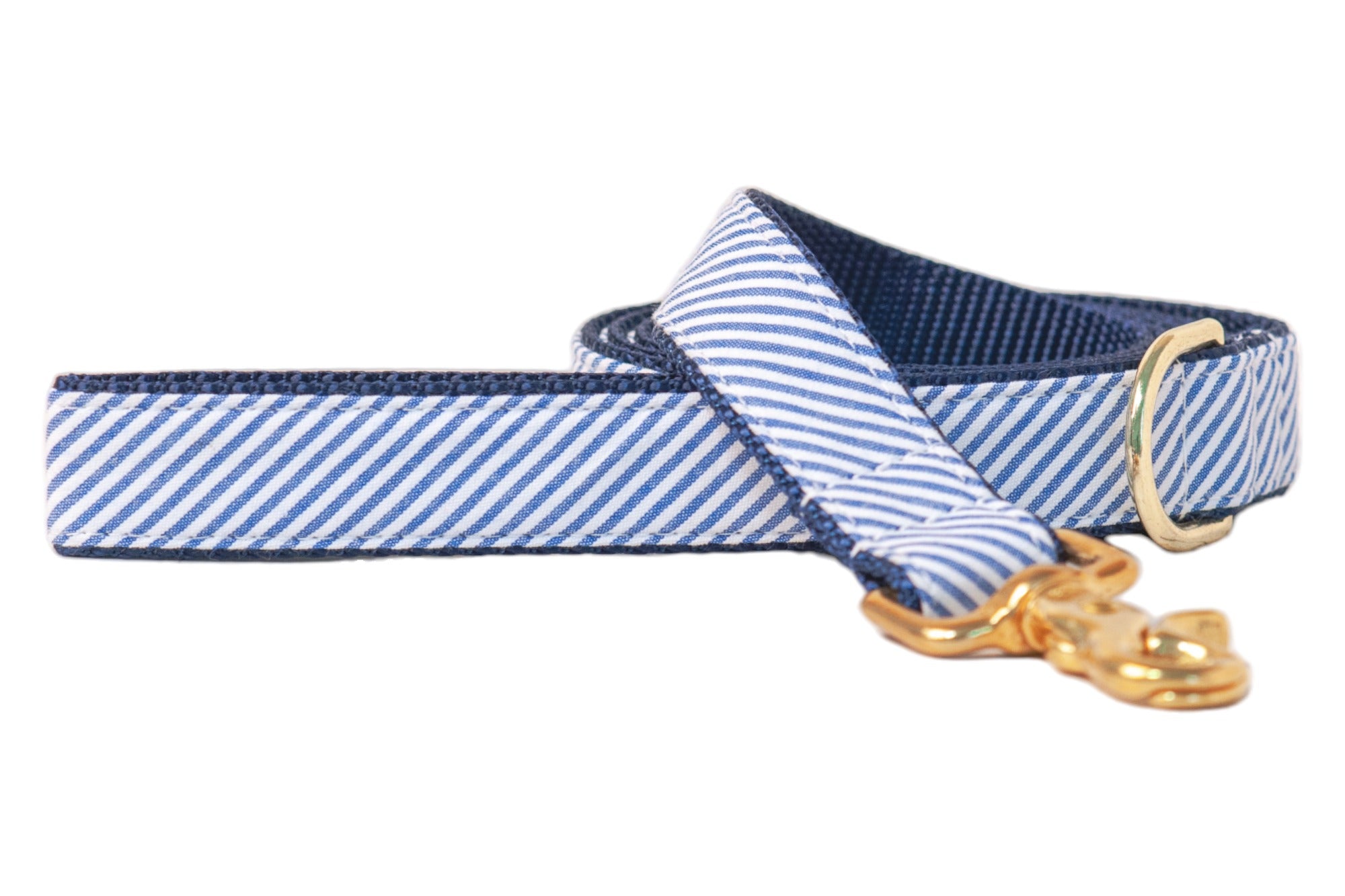 A stylish dog leash made from seersucker with a diagonal blue and white striped pattern. The leash features a dark blue webbed interior for durability and structure. It is finished with polished gold-tone hardware, including a swivel clasp and a D-ring near the handle for accessory attachment or waste bag holders. The overall design is clean, nautical-inspired, and refined.