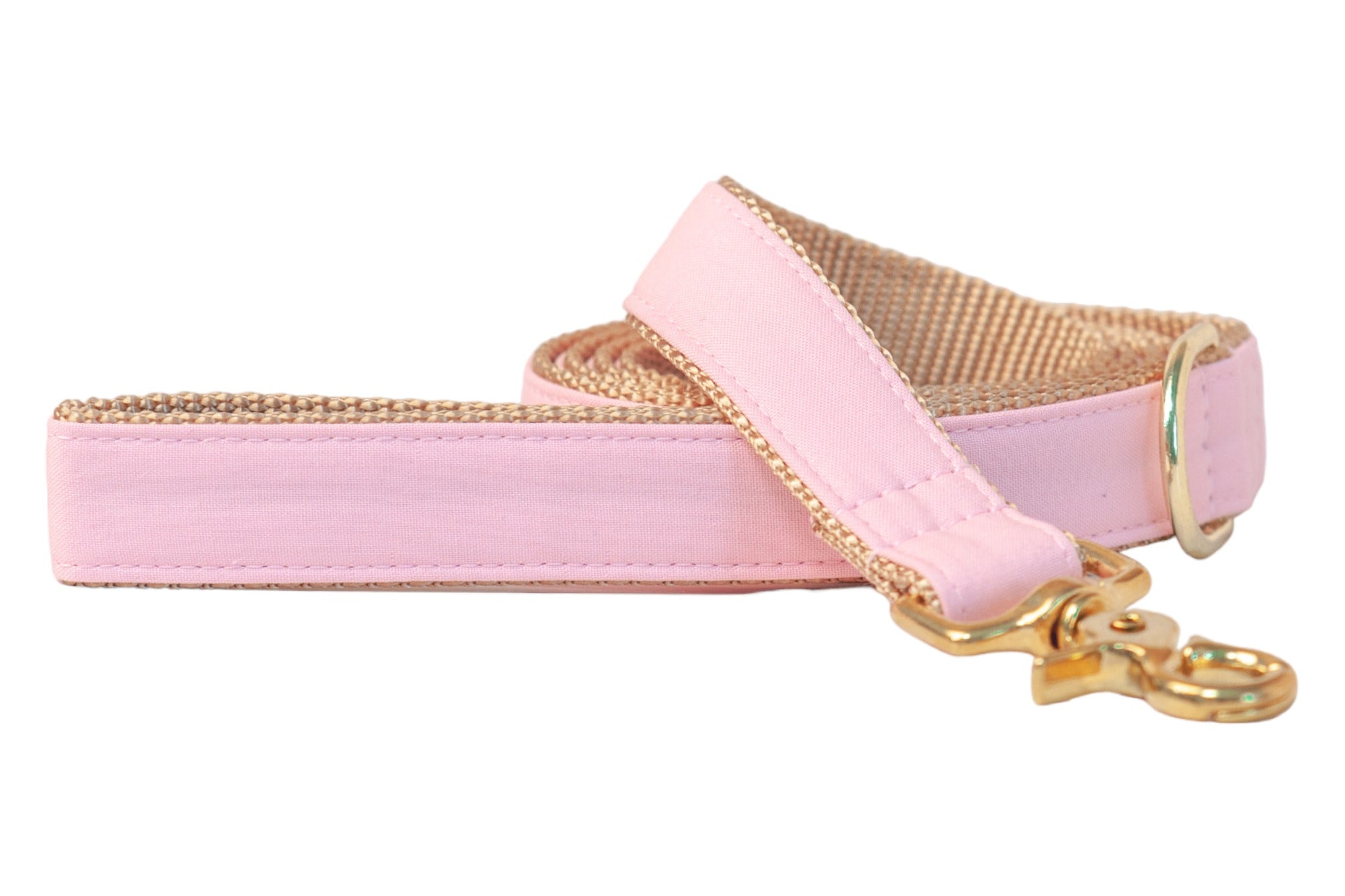 A coiled dog leash with a pink fabric outer layer and tan woven underside, finished with polished gold hardware including a swivel clip and D-ring, displayed against a white background.