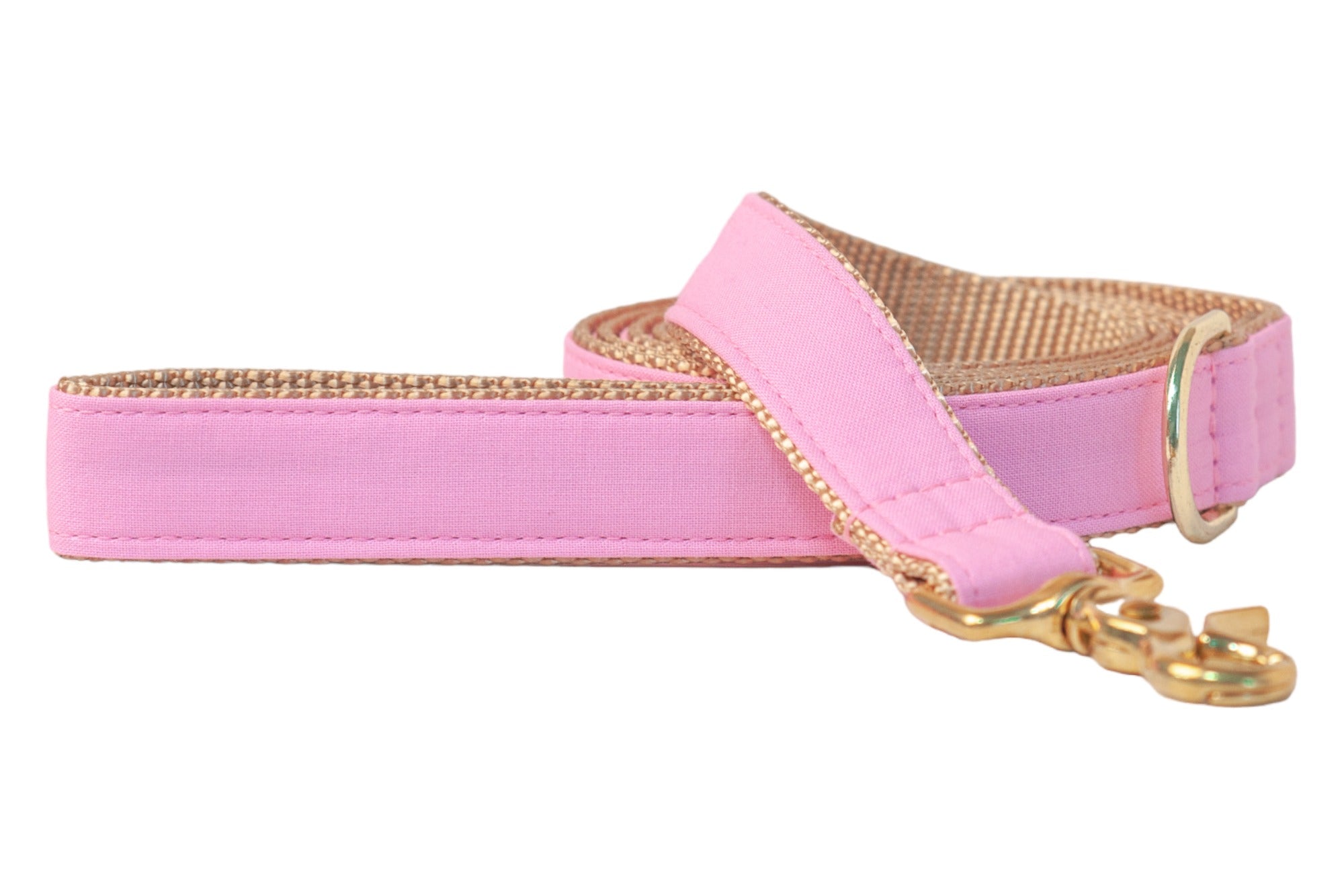 Pink fabric dog leash with a durable tan nylon backing and shiny gold metal hardware. The dog leash is coiled with the clasp and D-ring visible at the front.