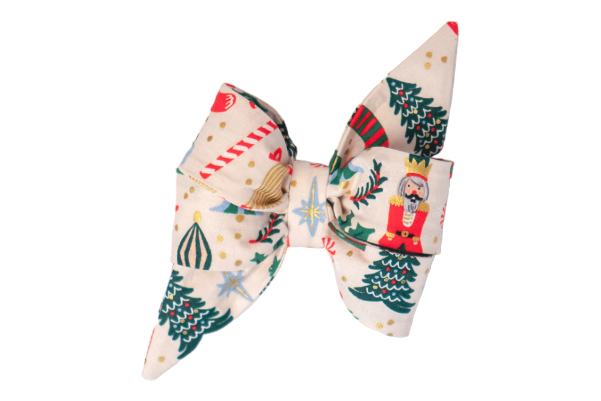 A festive dog belle bow with pointed ends, made from cream-colored fabric featuring a whimsical multi-colored holiday pattern. The design includes nutcrackers, Christmas trees, candy canes, ornaments, metallic dots, and gift boxes in red and green tones.