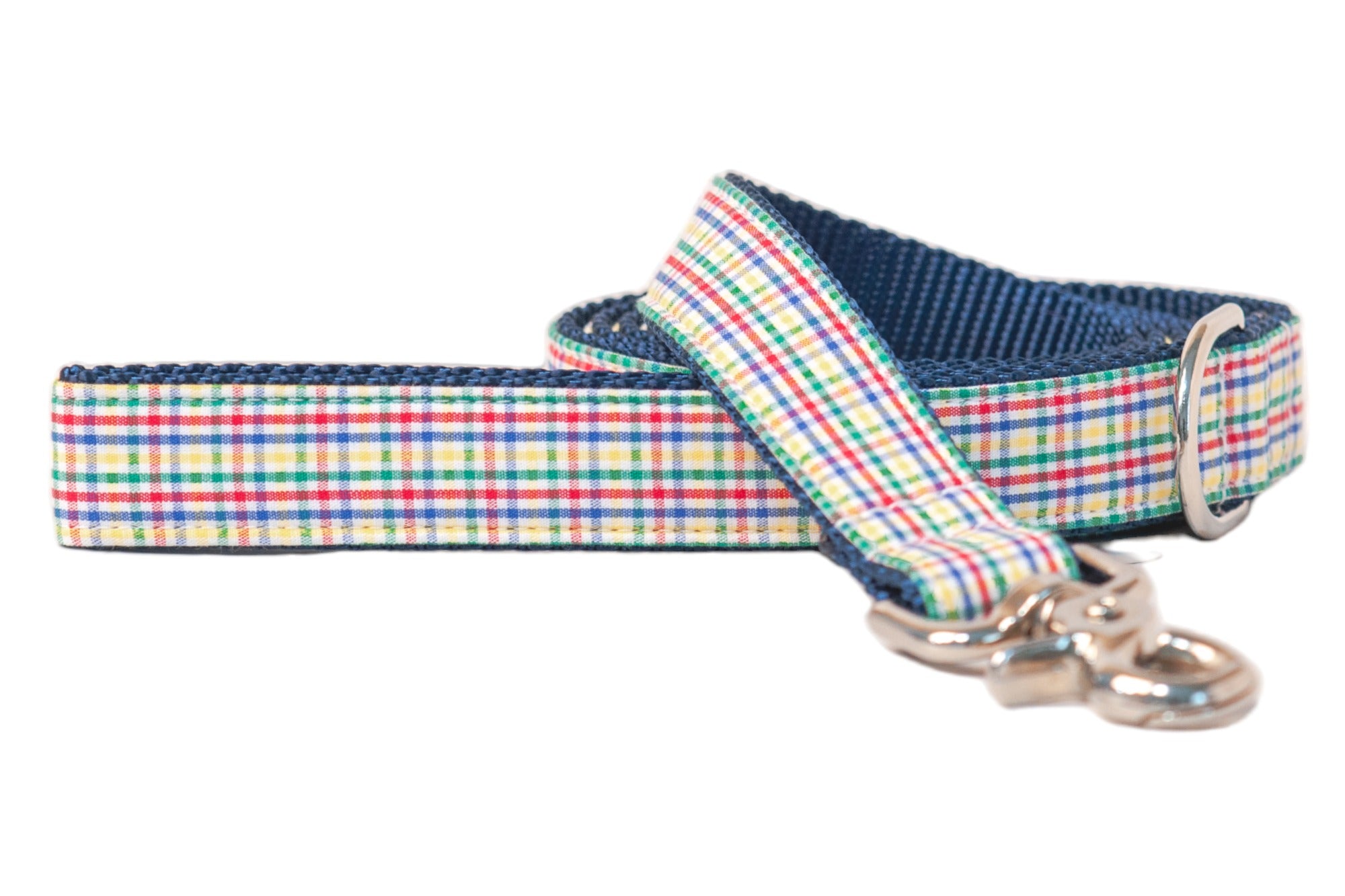 Close-up of a colorful plaid dog leash featuring a checkered pattern in primary colors, reinforced with nylon backing. The end of the leash has a sturdy metal clasp and a small D-ring loop.