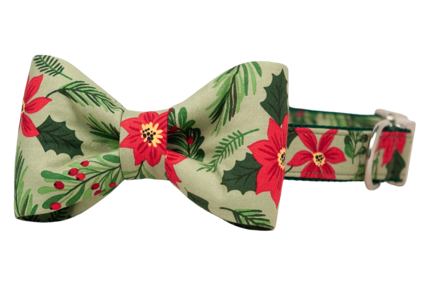 A festive dog collar with an attached bow tie, both made from matching light green fabric featuring poinsettias, pine needles, holly leaves, and berries. The bow tie is neatly centered and symmetrical, adding a playful holiday accent to the structured collar, which includes a buckle and adjustment hardware.