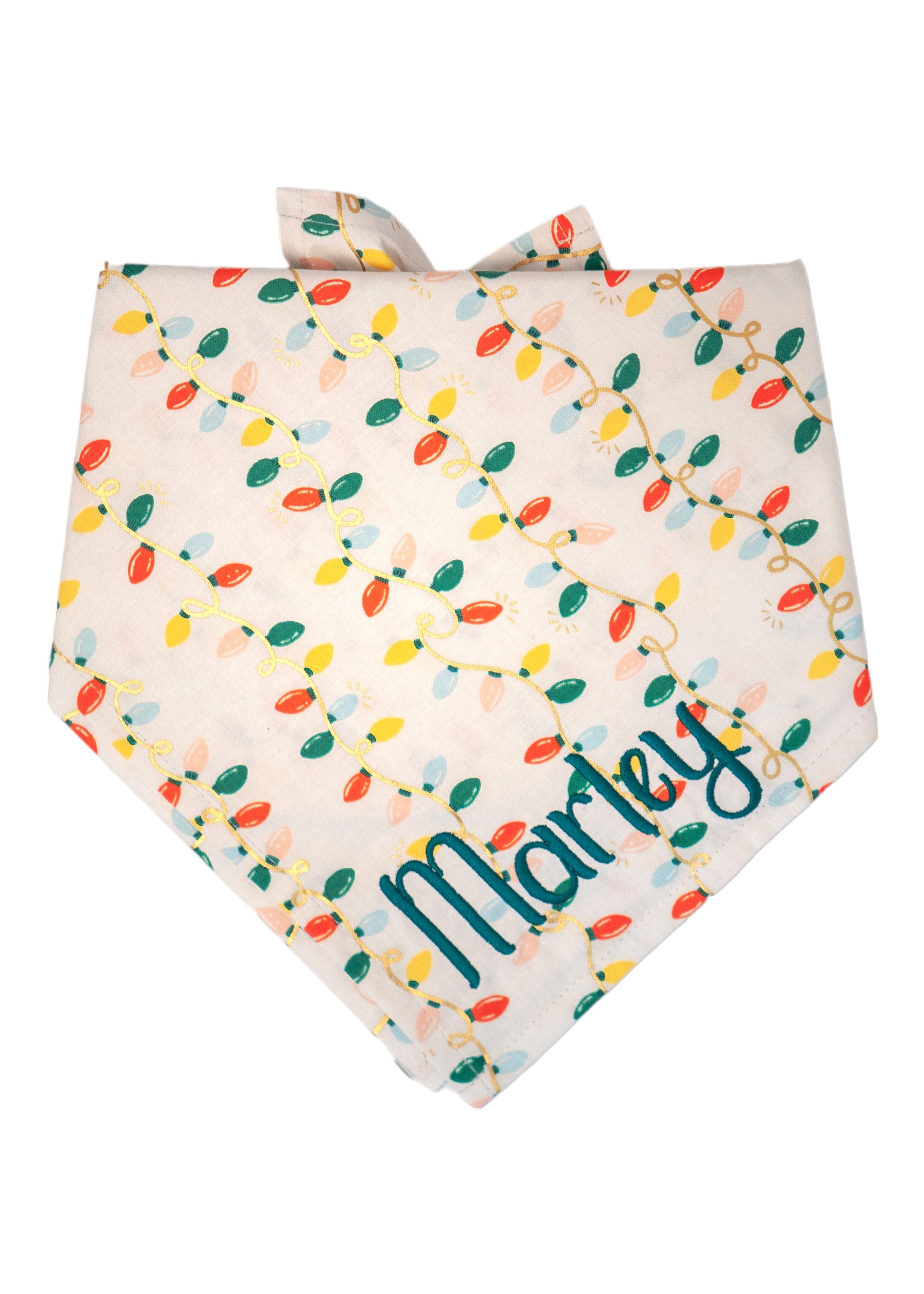 A holiday-themed dog bandana with a cream-colored background and a repeating print of colorful Christmas string lights. The bulbs are red, green, yellow, blue, and peach, connected by looping cords arranged diagonally across the fabric. The bandana ties at the top and has a classic look. The name "Marley" is embroidered in the bottom right.