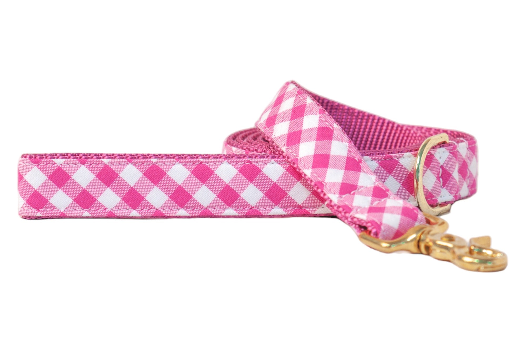 Fuchsia and white plaid dog leash with a classic checkered fabric exterior and sturdy webbed interior. Features a gold-tone metal clasp and D-ring for secure attachment and added style.