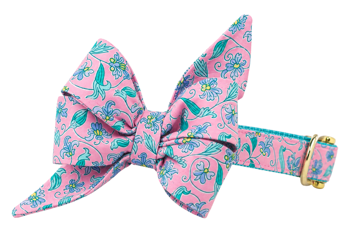 Dog collar featuring a large belle bow in Garden Gate fabric, a pink print with teal and periwinkle blue flowers and vines, attached to a matching Garden Gate collar with a nylon inner lining and gleaming gold hardware, including a D-ring and buckle.