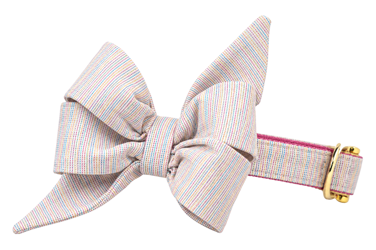 Dog collar featuring a large belle bow in Gotcha Glitter fabric, an oatmeal woven fabric with pastel glitter threads, attached to a matching Gotcha Glitter collar with a nylon inner lining and gleaming gold hardware, including a D-ring and buckle.