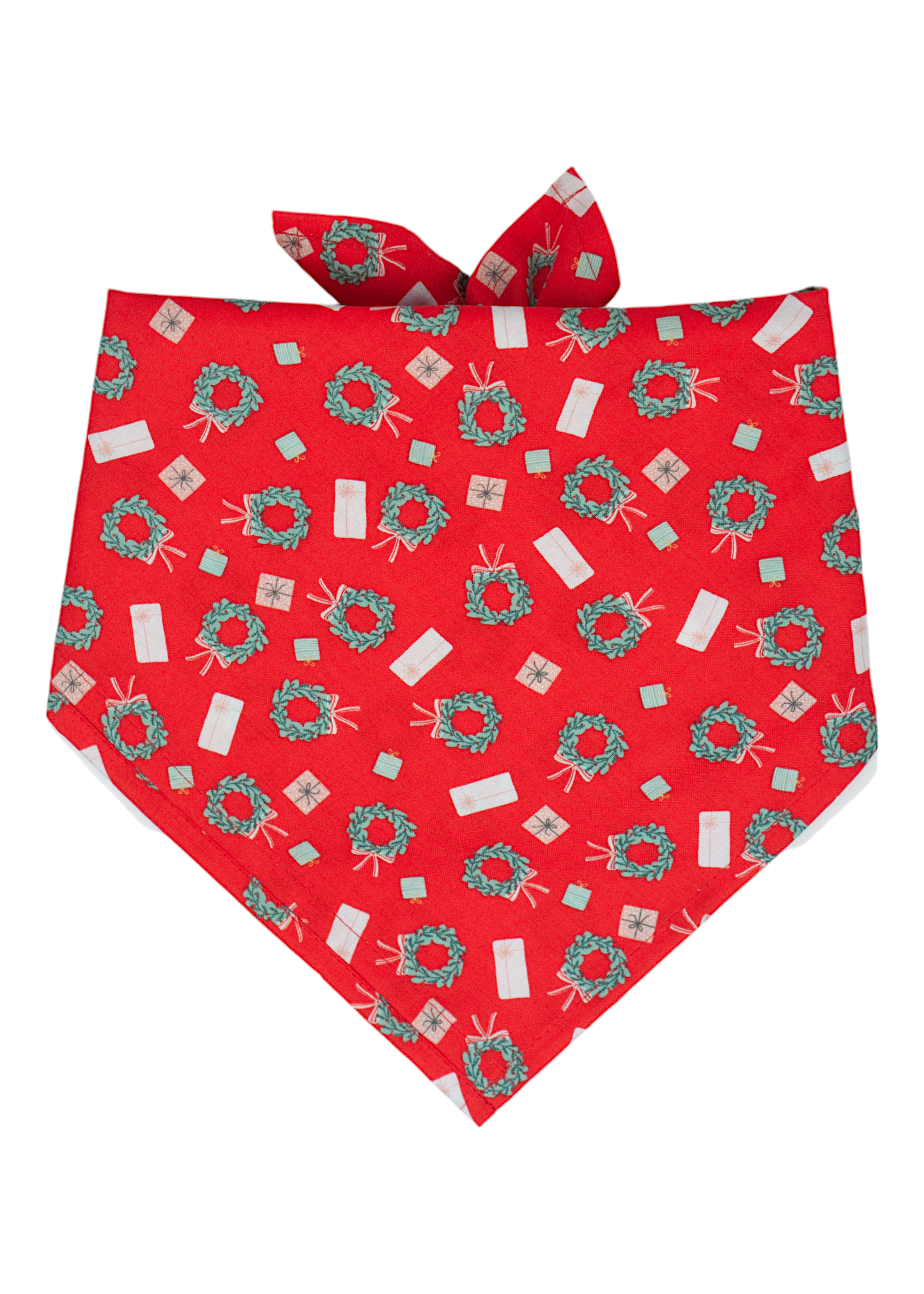 Festive dog bandana made from bright red fabric, with a repeating pattern of holiday wreaths and gift boxes. The bandana is tied at the top and drapes to a centered point, perfect for seasonal wear.