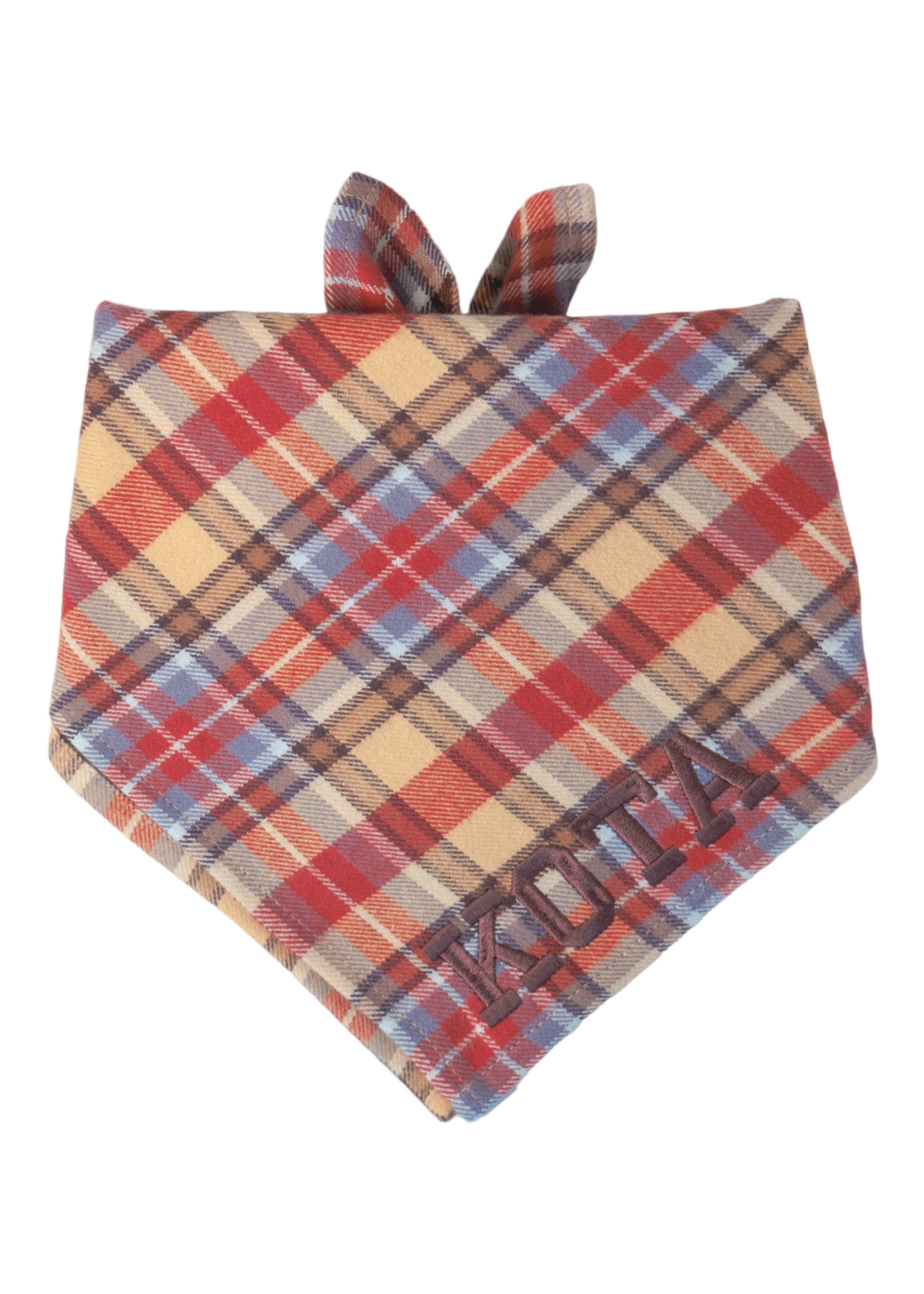 Cozy plaid dog bandana in warm fall hues, crafted from flannel fabric and accented with the name “KOTA” embroidered in dark thread at the bottom.