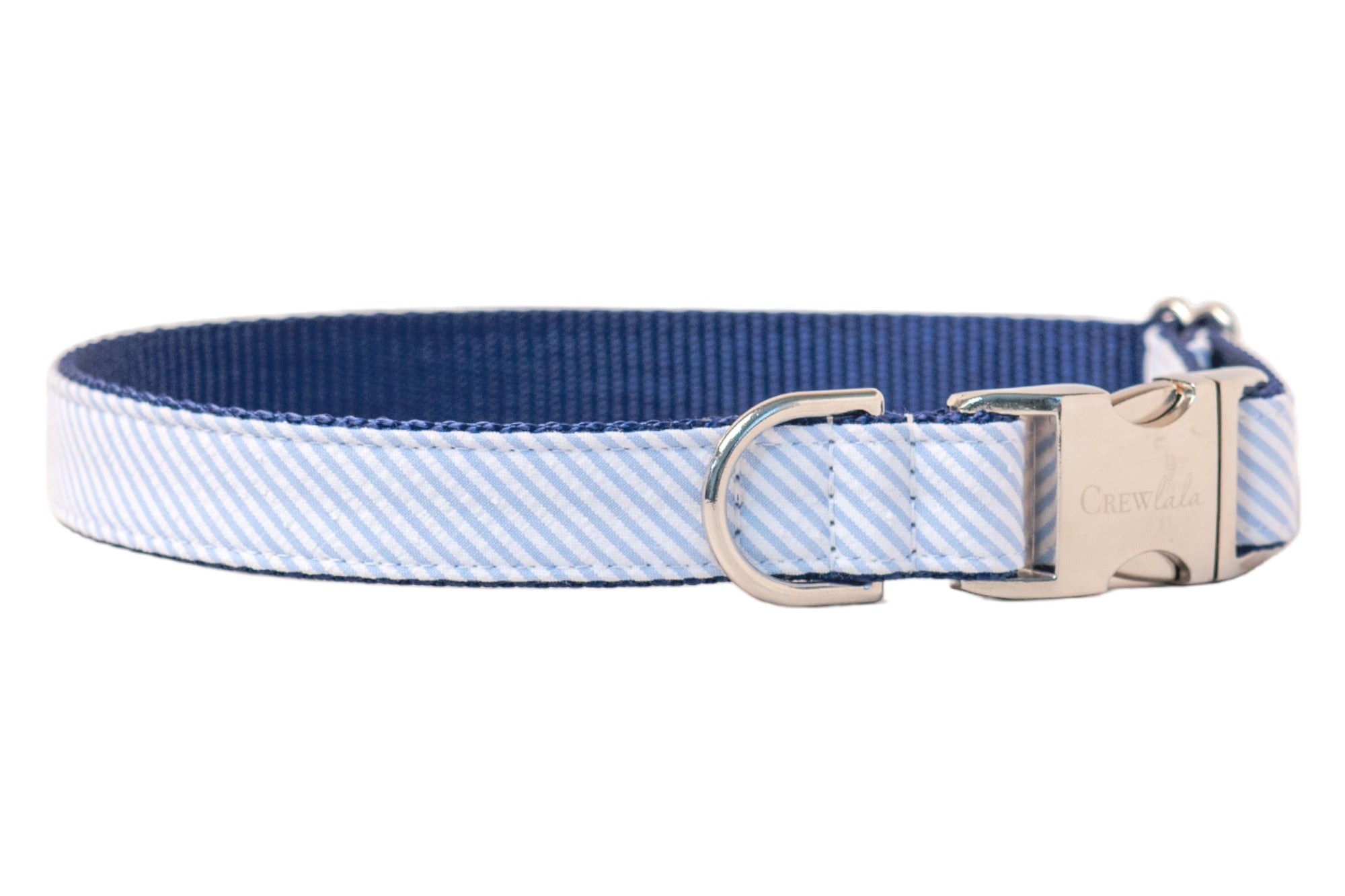 A dog collar with a preppy aesthetic, made of fabric featuring fine diagonal stripes in blue and white. The collar is reinforced with dark blue nylon and features shiny silver hardware, including a D-ring and a side-release clasp etched with the "Crew LaLa" logo.