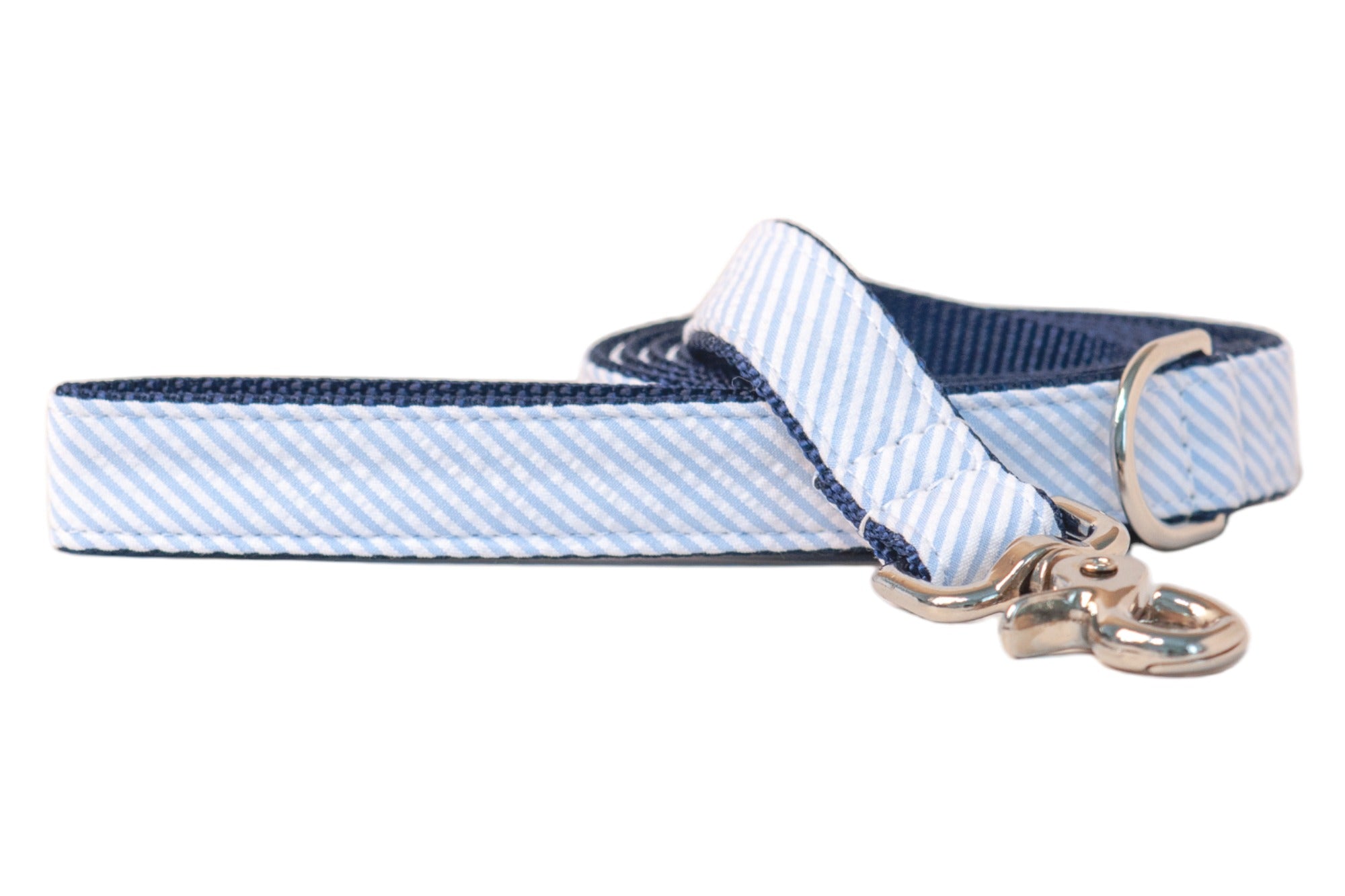A dog leash with a light blue and white seersucker fabric and a dark navy woven nylon interior for added durability. The leash features polished silver-tone hardware, including a swivel snap hook and D-ring, and is neatly coiled in the background for display.
