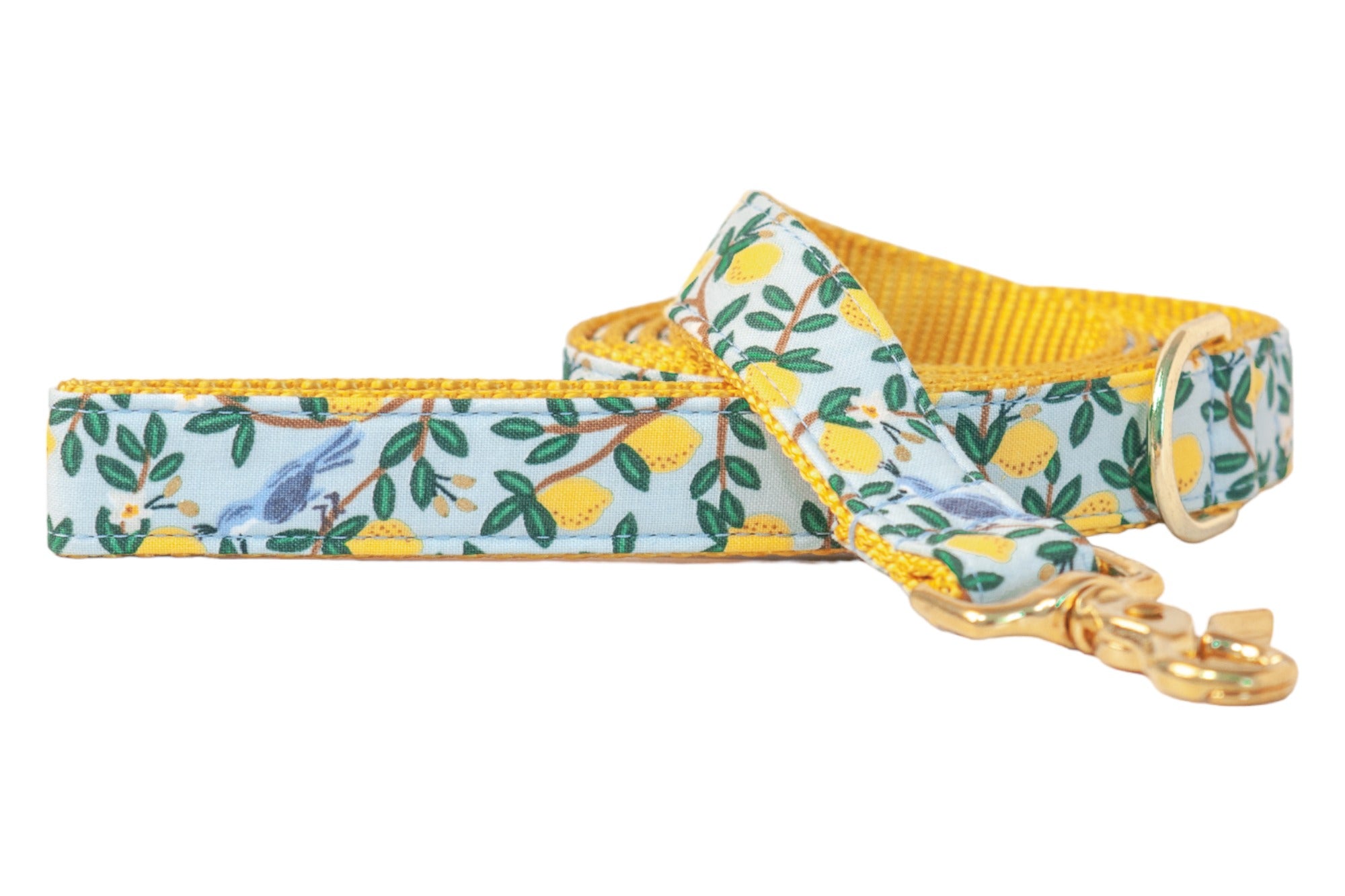 A stylish dog leash printed with a detailed pattern of yellow lemons and leafy branches, accented by blue birds. The inside lining is bright yellow, and it includes a shiny gold clasp and D-ring.