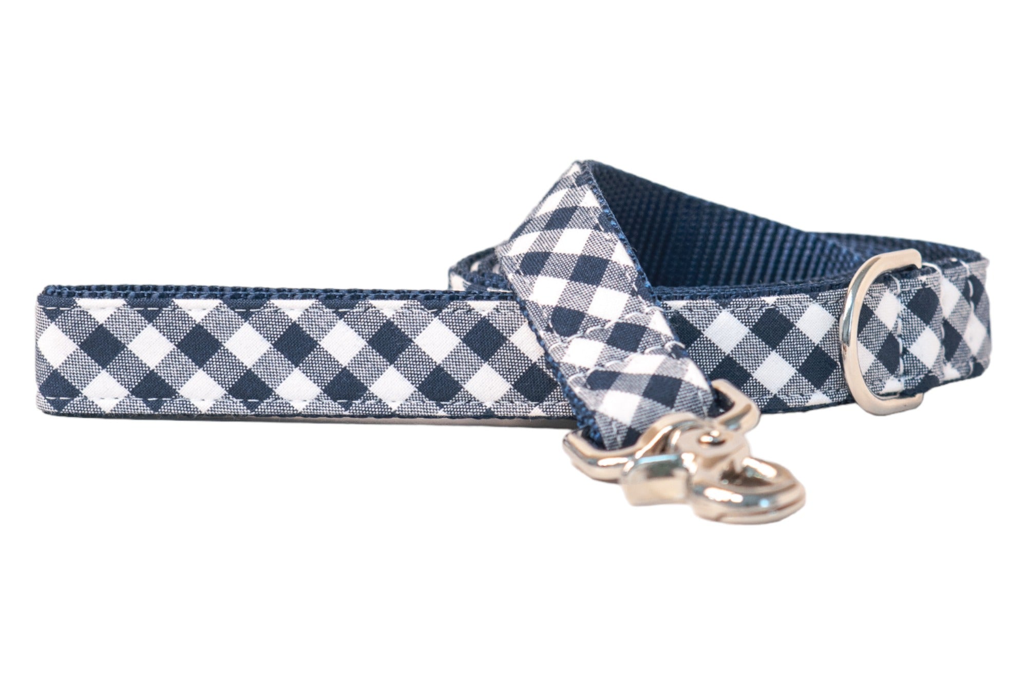 Navy plaid dog leash featuring alternating navy checks on cotton fabric sewn onto a dark blue nylon backing. The leash includes a shiny silver clasp for easy collar attachment and a matching D-ring stitched into the handle loop. The item is partially coiled in the photo, highlighting the flexibility and layered construction of the leash.