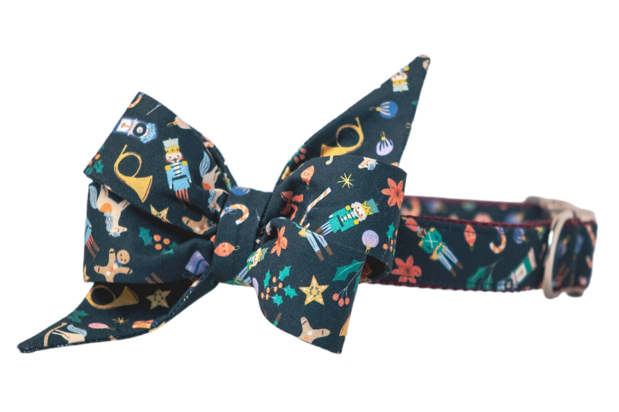 Festive dog collar featuring a large, structured belle bow with pointed ends. The navy fabric is covered in classic Christmas icons—nutcrackers, candy canes, gingerbread men, holly leaves, rocking horses, stars, and baubles. The collar includes metal hardware and a sturdy nylon webbing backing.