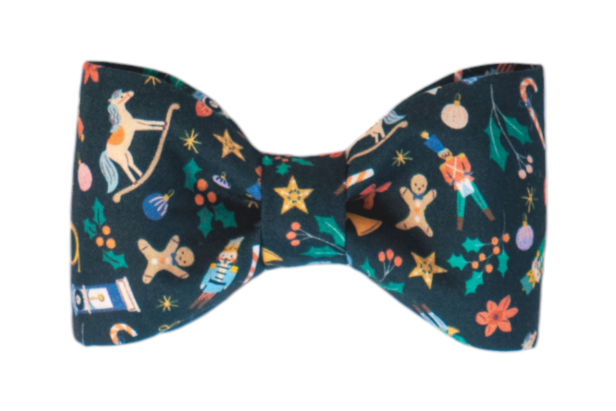 A festive dog bow tie made from dark blue fabric, featuring an intricate Christmas pattern with illustrated gingerbread men, nutcrackers, rocking horses, stars, holly leaves with berries, candy canes, baubles, and wrapped gifts in vibrant colors.