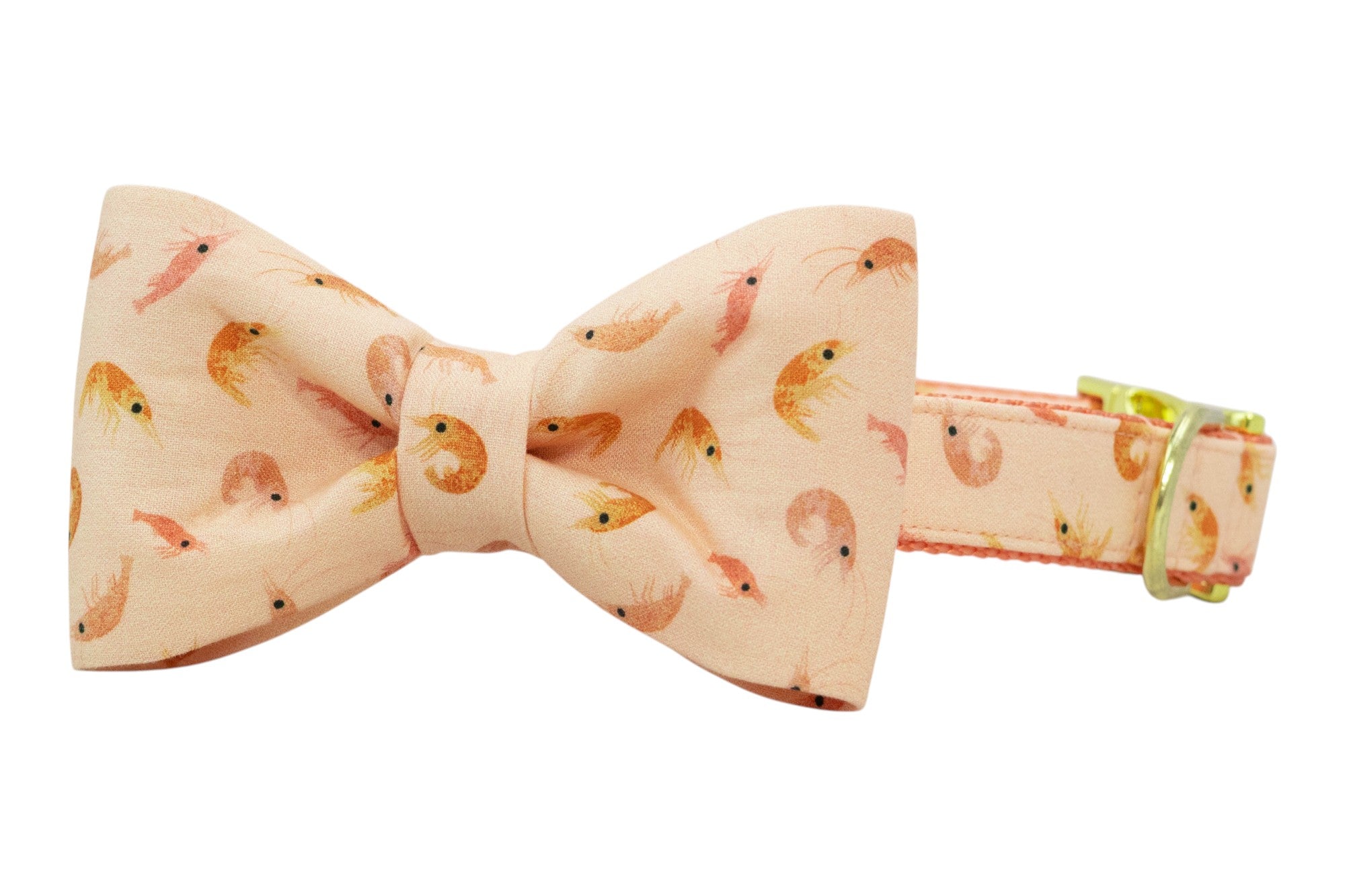 Peach-colored dog bow tie collar with a repeating shrimp pattern in soft pink and orange tones, attached to a matching adjustable collar with gold hardware.