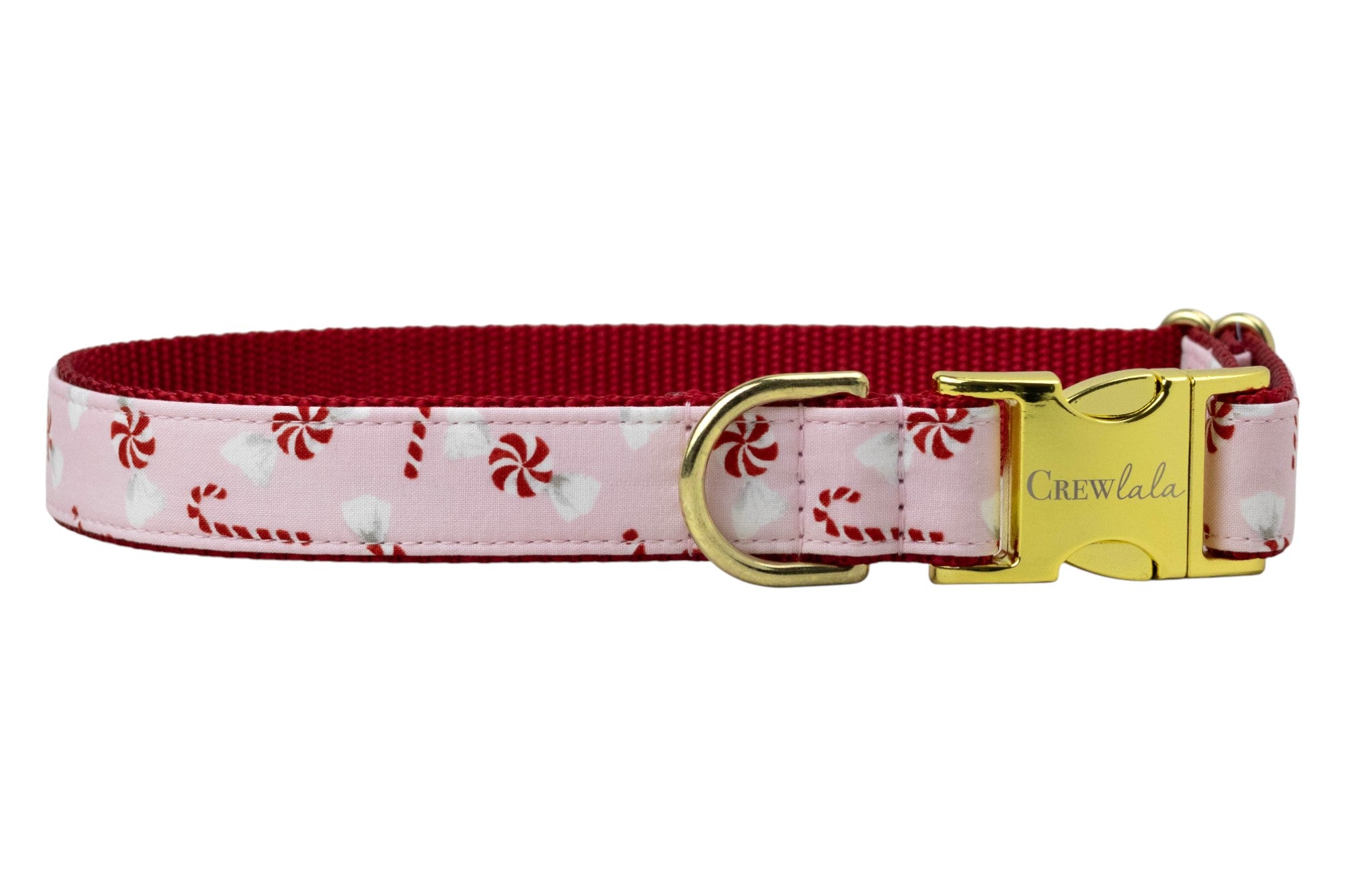 A festive dog collar made from light pink fabric with candy canes and peppermint swirl candies. The collar is backed with durable nylon webbing and features polished  hardware, including a D-ring and a side-release buckle engraved with the brand name "Crewlala."