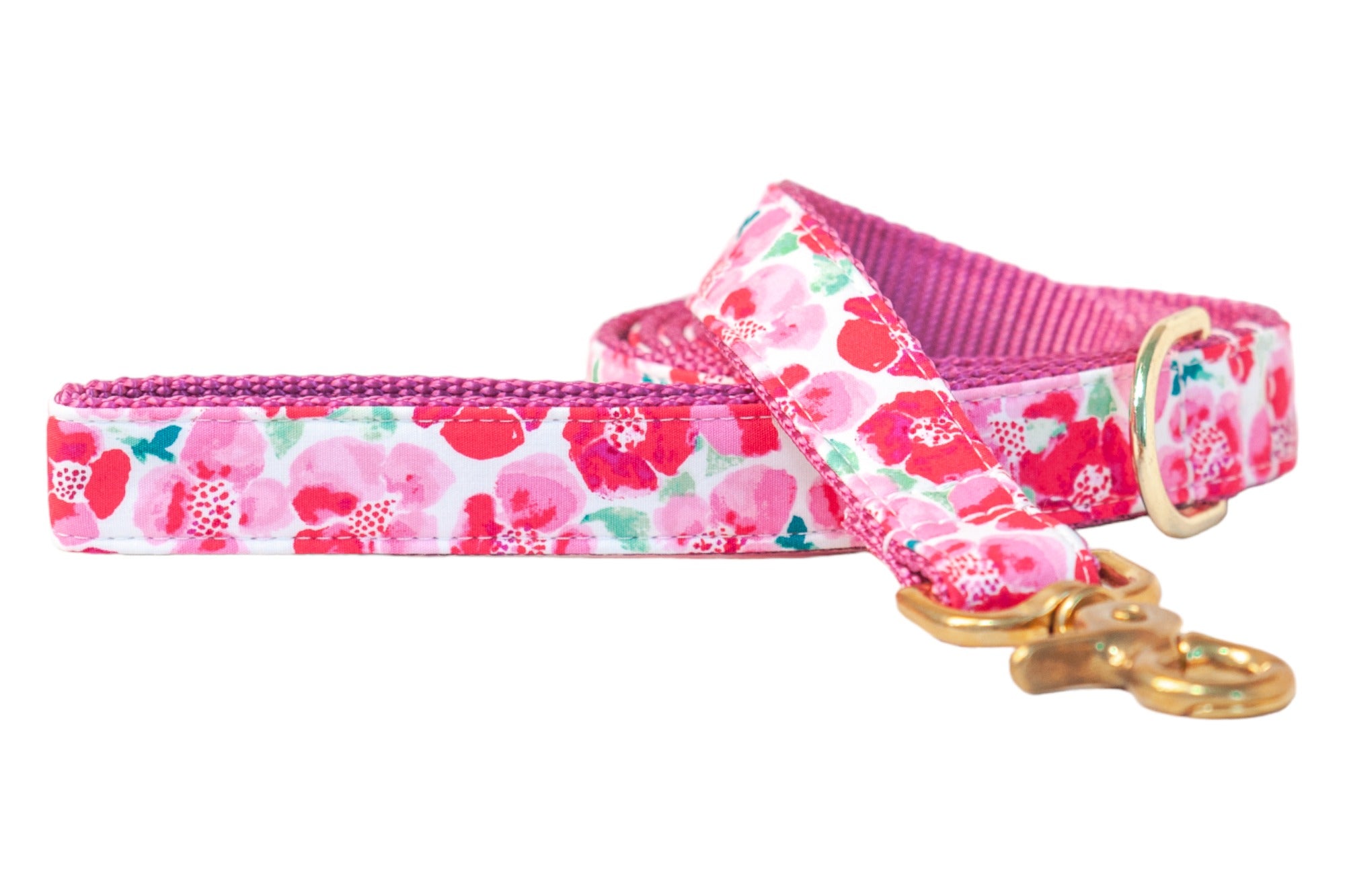 A charming dog leash wrapped in a playful floral pattern featuring watercolor-style blossoms in shades of pink, red, and coral with hints of green. The leash is lined with a fuchsia webbing for strength and contrast, and finished with polished gold-tone hardware for a cheerful, garden-party vibe.