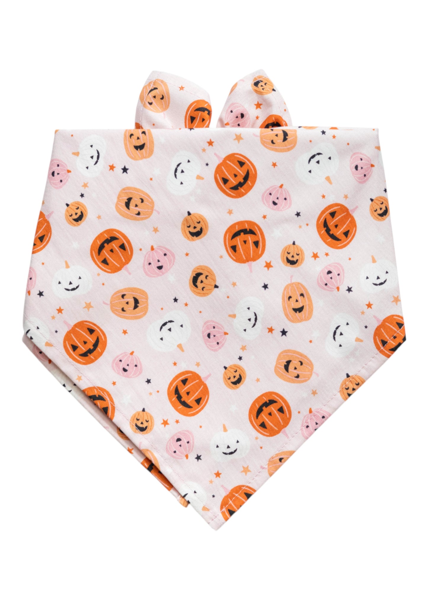 Halloween-themed dog bandana in a soft pink tone, folded into a triangle. The fabric is covered in a repeating print of smiling and spooky jack-o’-lantern faces, with assorted facial expressions, adding a whimsical and playful touch.