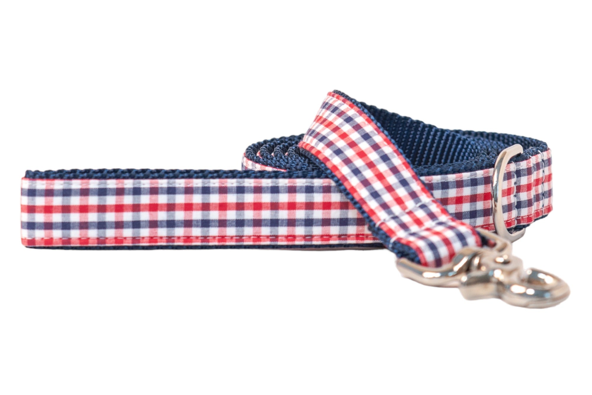 Dog leash with a red, white, and navy gingham check pattern on the outer fabric, contrasted with dark blue woven nylon lining for strength. The leash is partially coiled with a silver metal swivel clasp and D-ring visible near the handle. Neatly stitched edges in navy thread outline the structured design, all set against a white background.