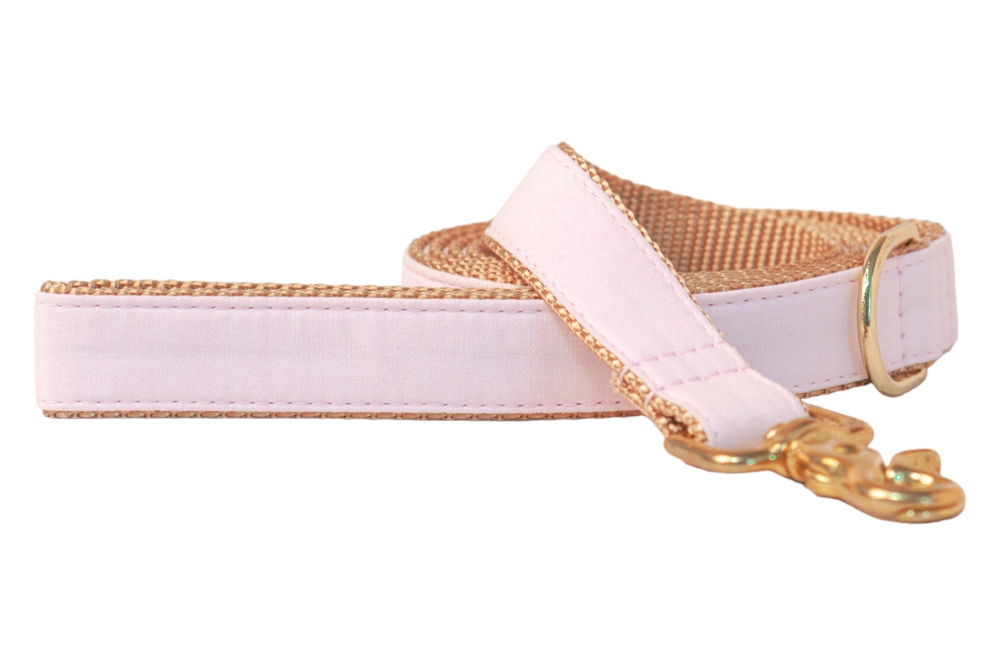 A handcrafted dog leash made from solid pale pink linen fabric layered over durable nylon webbing. The leash features reinforced stitching along the edges, a coordinating pink handle for comfort, and a polished metal swivel snap hook for secure collar or harness attachment. A matching gold D-ring sits near the handle for convenient accessory clipping.
