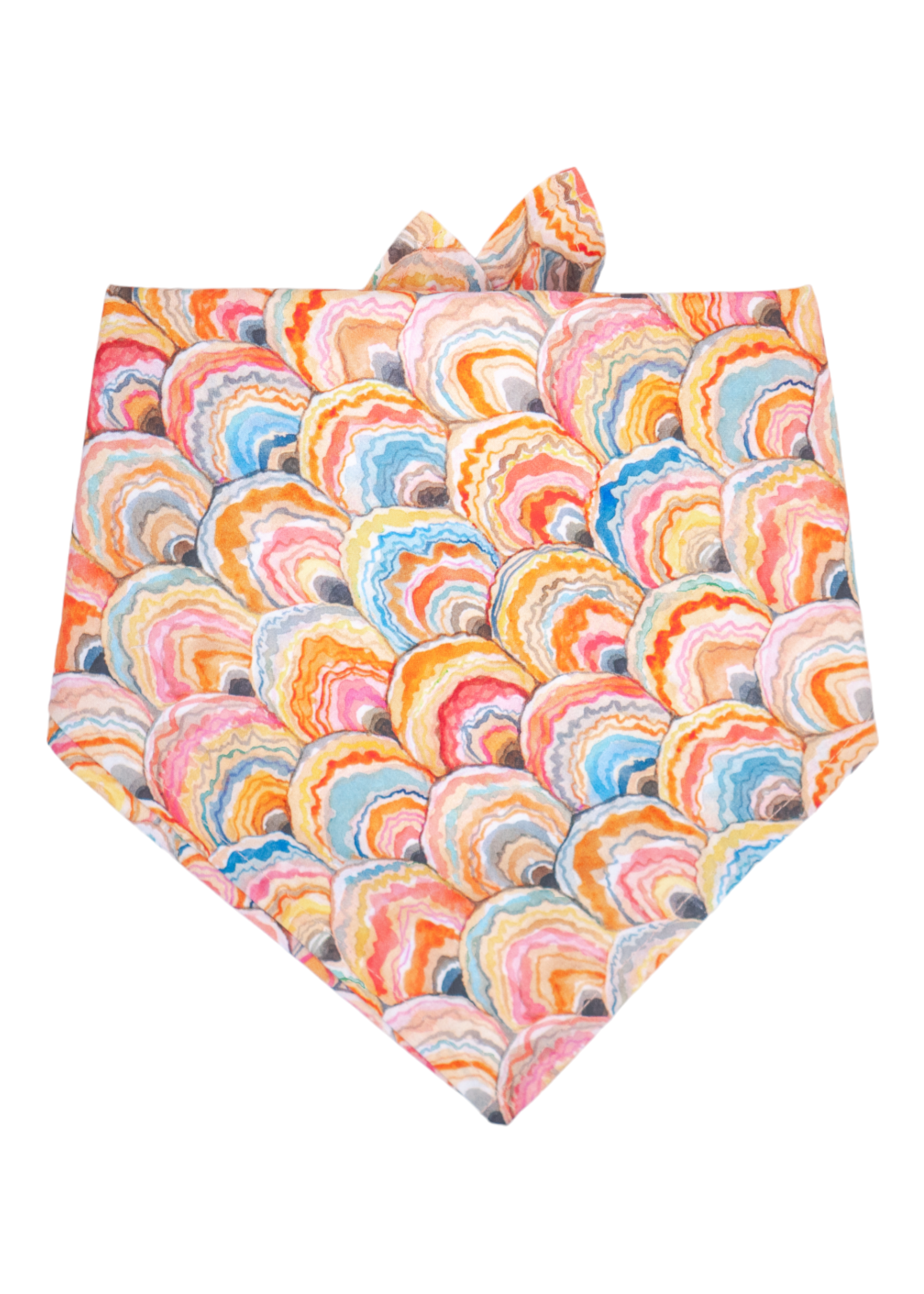 A colorful dog bandana featuring a scalloped shell pattern in a hand-painted style, with overlapping swirls of orange, pink, blue, and yellow. The fabric is folded into a triangular shape with tie ends visible at the top.