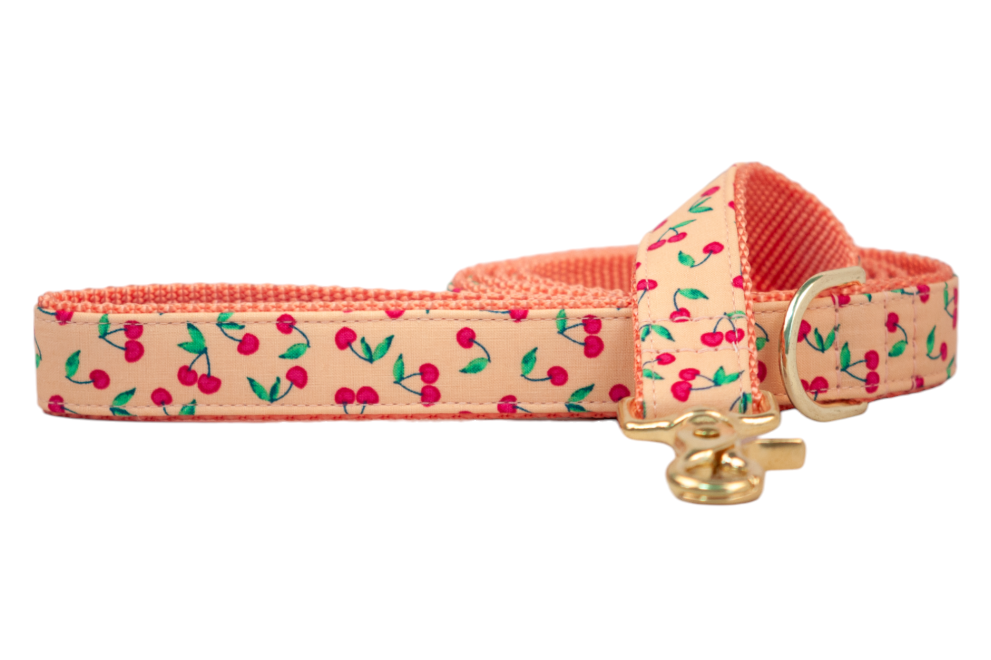 A fabric dog leash in a cheerful cherry print, with red cherries and green leaves scattered across soft peach fabric. The leash includes a bright gold clasp and durable orange webbing, blending whimsical design with sturdy functionality.