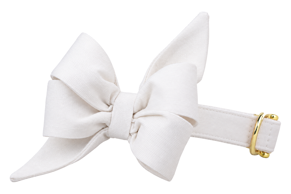 Dog collar featuring a large belle bow in White Wedding Woven fabric, a solid white woven fabric, attached to a matching White Wedding Woven collar with a nylon inner lining and gleaming gold hardware, including a D-ring and buckle.