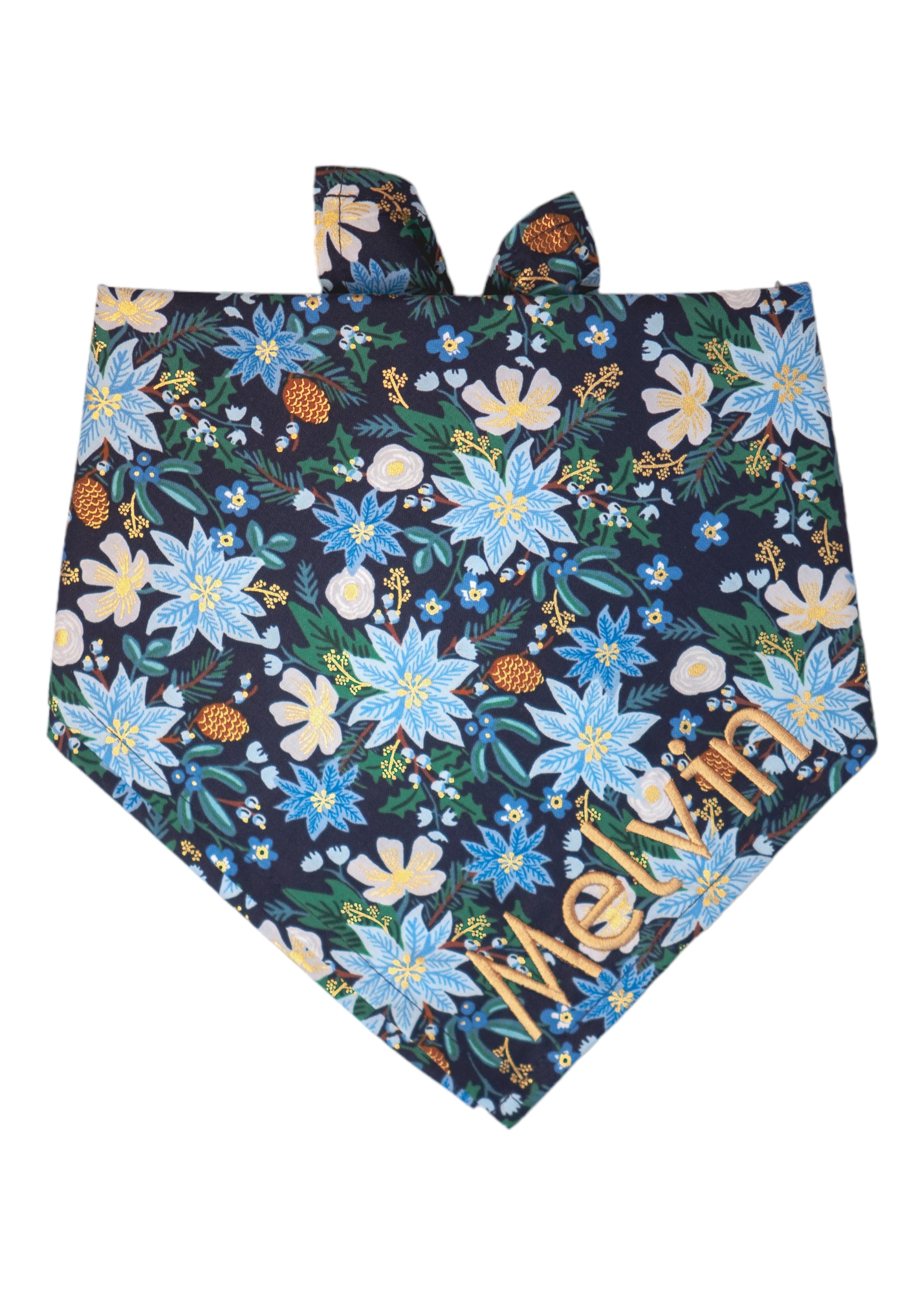 A winter-themed dog bandana featuring a dark navy blue background with an all-over print of icy blue poinsettias, pale flowers, blossoms, pinecones, fir branches, and delicate metallic accents for a festive holiday look. The name "Melvin" is embroidered on the bottom right.