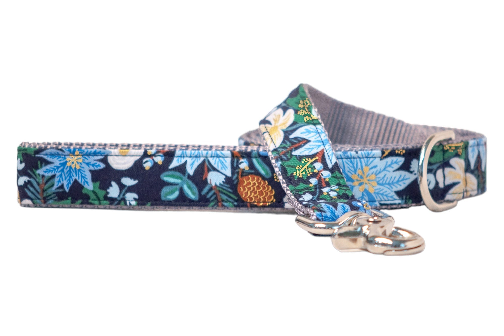 A winter-themed dog leash made from navy blue fabric with a festive floral pattern. The design includes light blue poinsettias, light colored flowers, pinecones, leaves, and metallic accents. The leash features a metal clasp and a nylon webbing interior for added durability.