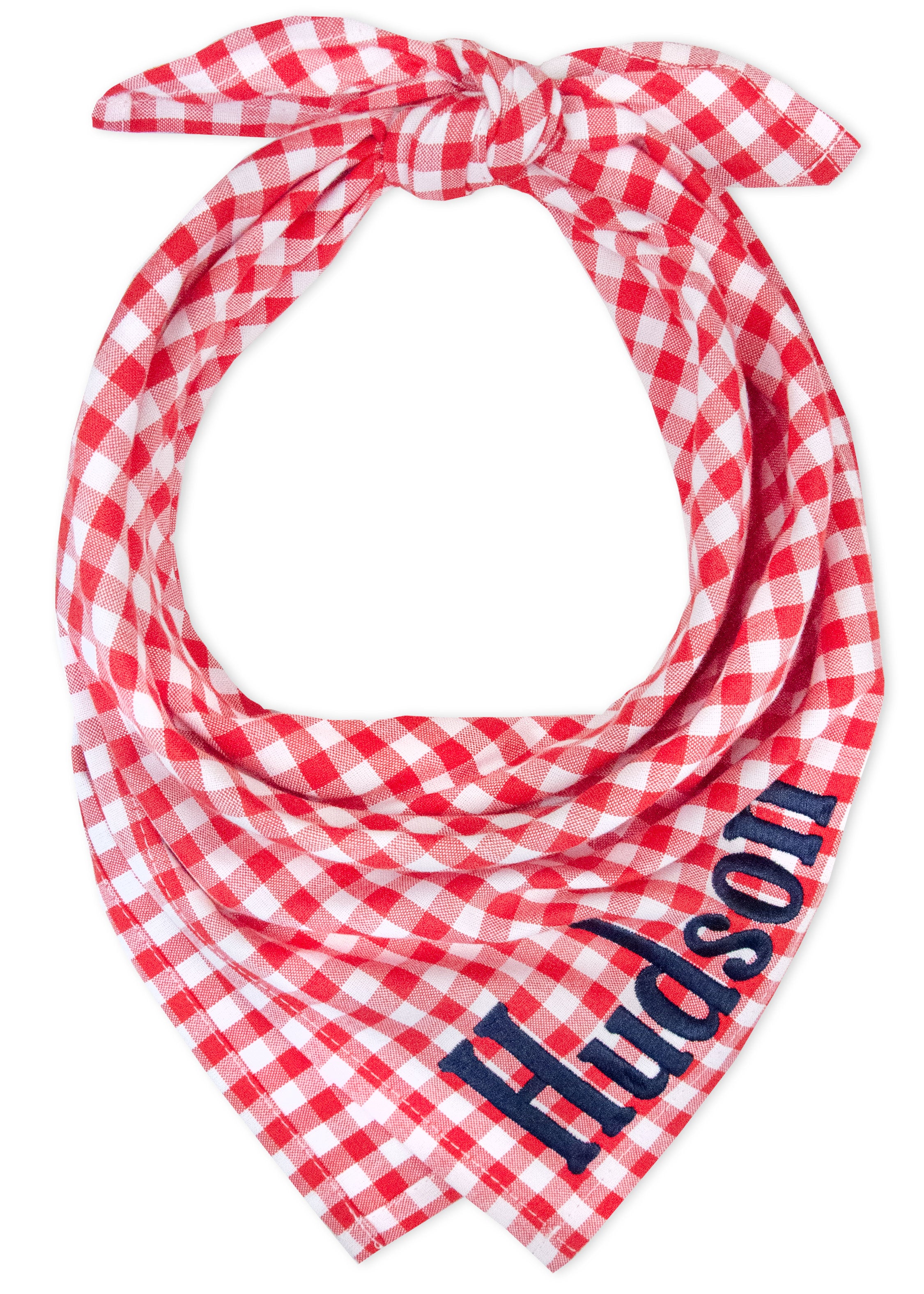Classic dog bandana made from red and plaid fabric with "Hudson" embroidered on it. Two narrow tie ends peek out at the top, giving the piece a secure, adjustable fit.