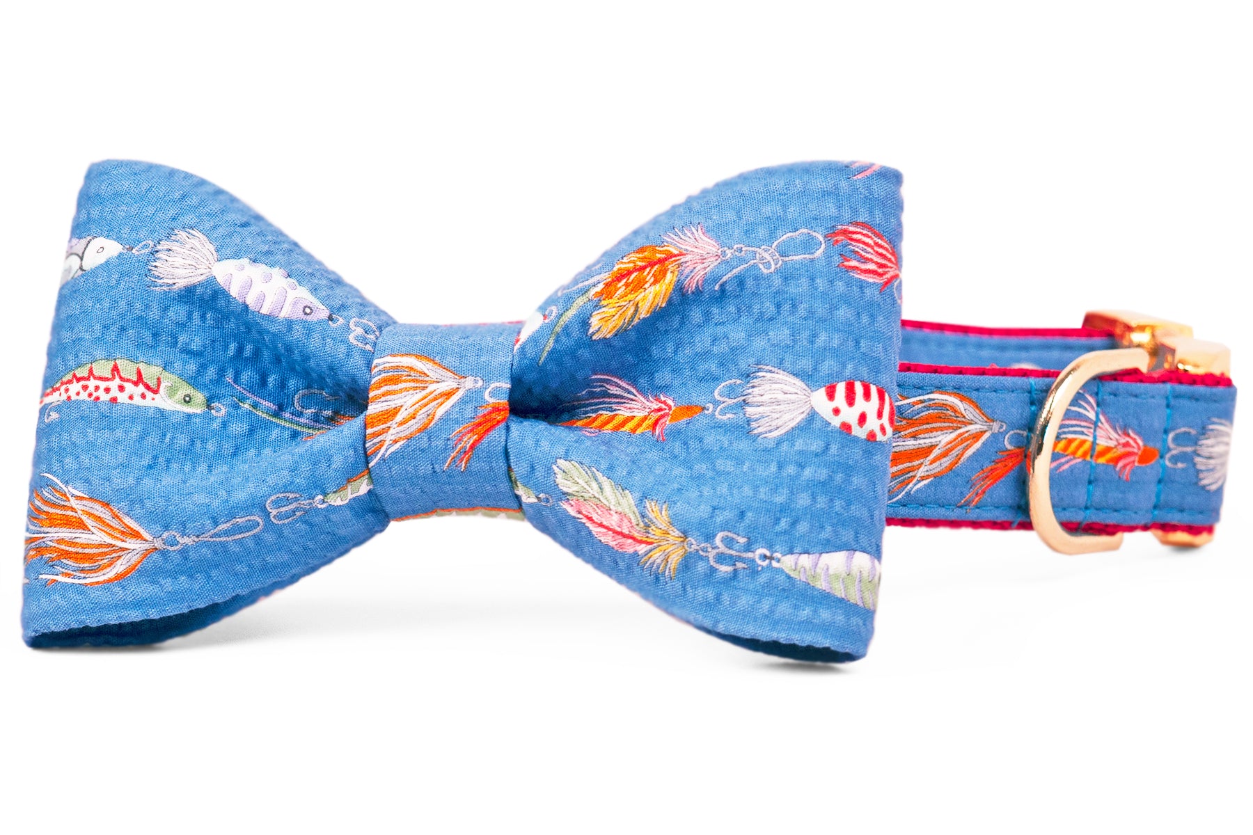 Vibrant dog bow tie collar featuring a nautical fishing lure print on blue seersucker-style fabric. The oversized bow tie is centered on a matching collar with red webbing and gold-tone hardware, including a polished D-ring for leash or tag attachment.