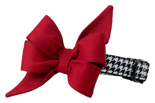 A stylish dog collar featuring a bold black and white houndstooth fabric overlay and an attached feminine red belle bow. The belle bow is made from structured cotton with crisp, voluminous loops and sharply pointed tails, creating a dramatic and elegant silhouette. The collar includes black metal hardware and an adjustable strap, combining classic sophistication with playful charm—ideal for formal events, game day, holiday photos, or seasonal wear.
