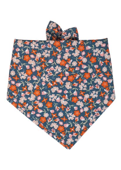 Dog bandana made from smooth cotton fabric with a colorful flower pattern featuring blooms on a dark blue base. The bandana is neatly hemmed, folded , and is designed to be tied at the top for securing around your pup's neck.