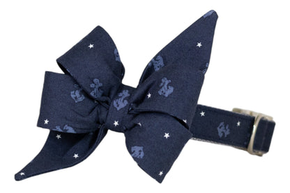 Navy blue dog collar adorned with a matching fabric bow decorated with white stars and light blue anchors. The collar is adjustable with a silver buckle.