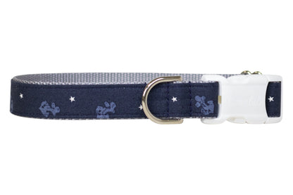 Nautical-themed navy blue dog collar featuring light blue anchor designs and white stars, finished with a polished metal D-ring and and white buckle.