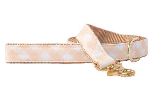 A neatly rolled dog leash featuring an apricot and white checkered pattern, tan interior webbing, and gold-tone metal accents—perfect for pups with a taste for sweet, classic style.