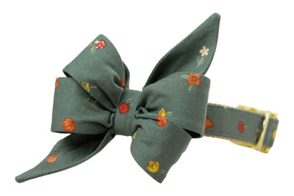 Chic dog collar with a large, matching, double-layered bow in green fabric, patterned with vibrant fall illustrations like berries, sunflowers, and leaves. Designed for eye-catching seasonal photos and festive outings, with sturdy construction and luxe buckle.
