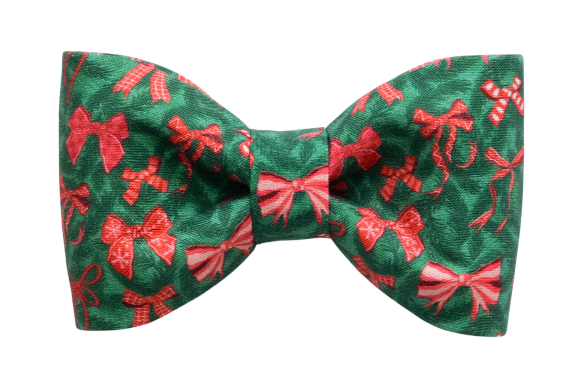 A festive dog bow tie made from green fabric with an all-over print of bows, candy canes, and ribbon designs. The bow tie has a symmetrical, classic shape with a gathered center and is designed to be a cheerful holiday look.
