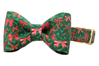 Holiday-themed dog collar with a neatly shaped, matching green bow tie attached at the center, with an all-over pattern of bows and candy canes. The collar is constructed with nylon webbing for durability and finished with metal hardware, giving it a polished seasonal look.