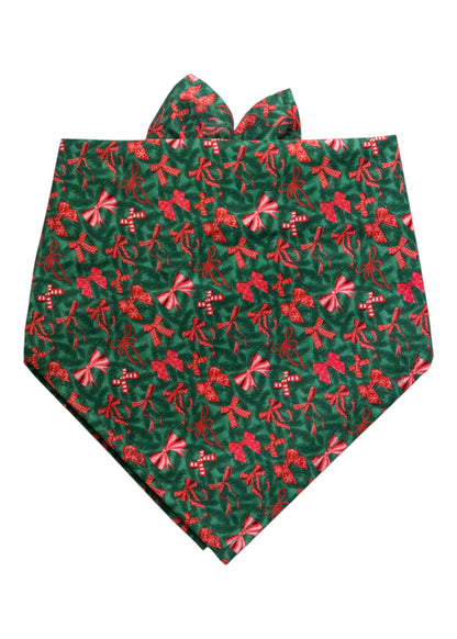 Festive green dog bandana adorned with a repeating holiday print of bows, along with small candy cane shapes. The bandana is folded into a classic triangle with two top extensions for tying, giving it a decorative and seasonal look.