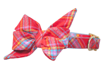 Bright red dog collar with an attached, matching, flannel belle bow in a vivid plaid print. The belle bow is large and structured, with pointed ends extending outward. The collar features a shiny metal clasp for closure.
