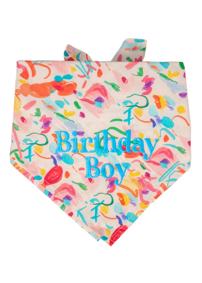 Colorful dog bandana with an abstract confetti-like pattern in bright hues and the words “Birthday Boy” embroidered in bold blue lettering.