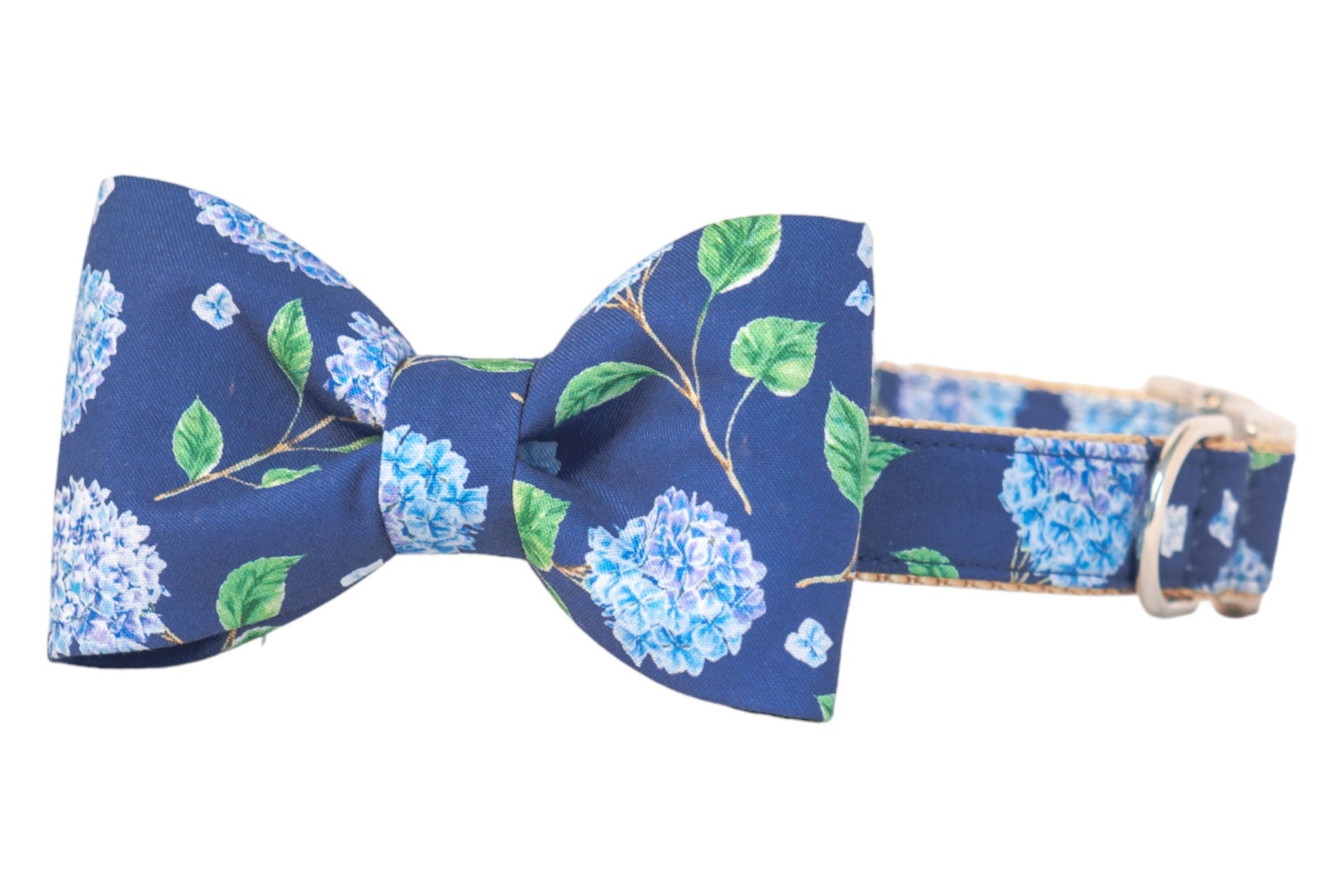 Dog collar with an elegant bow tie, both covered in a botanical hydrangea print on a deep navy background. The soft fabric features detailed leaves and pale blue flowers, and the collar includes metal hardware for attachment.