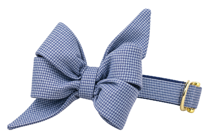 Dog collar featuring a large belle bow in Blue Houndstooth fabric, a fine periwinkle blue and white mini houndstooth check, attached to a matching Blue Houndstooth collar with a nylon inner lining and gleaming gold hardware, including a D-ring and buckle.
